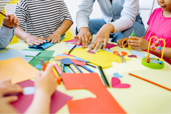 Children and an adult creating crafts with paper, scissors, glue, and colorful art supplies.