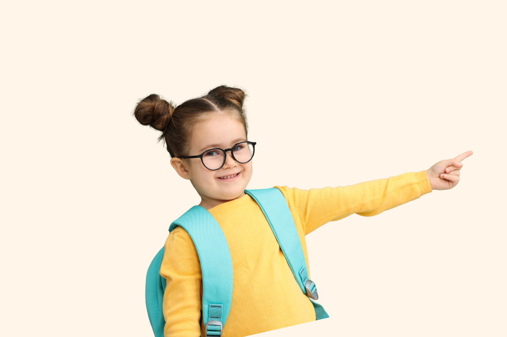 A young girl with glasses wearing a yellow sweater and a blue backpack, smiling and pointing to the right.