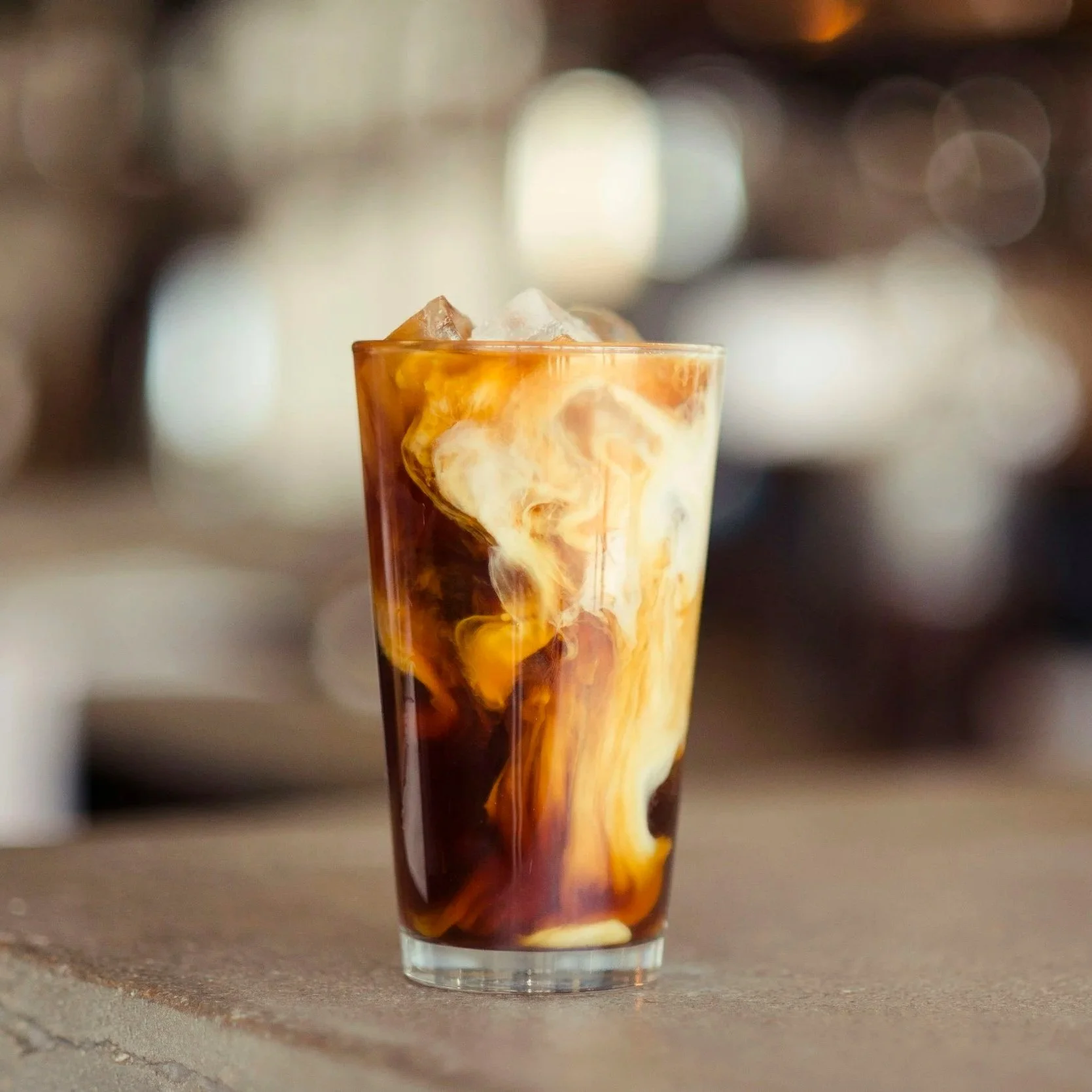 A tall glass filled with iced coffee and cream swirling together, creating a marbled effect.