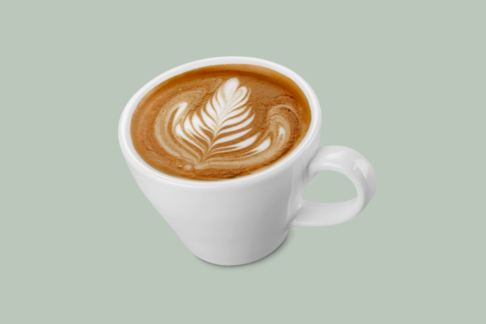 White mug filled with latte coffee featuring leaf latte art design on top, set against a light green background.