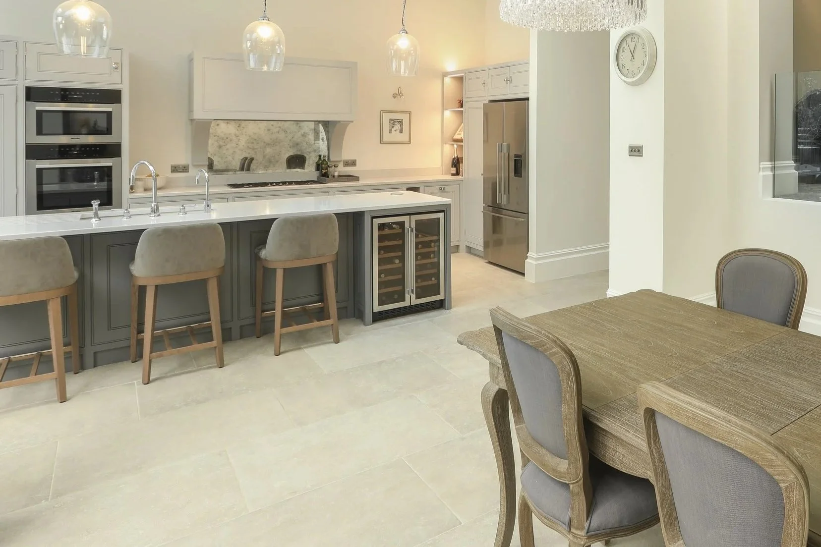 Modern kitchen with island, three barstools, stainless steel appliances, wine cooler, dining table, and chairs.