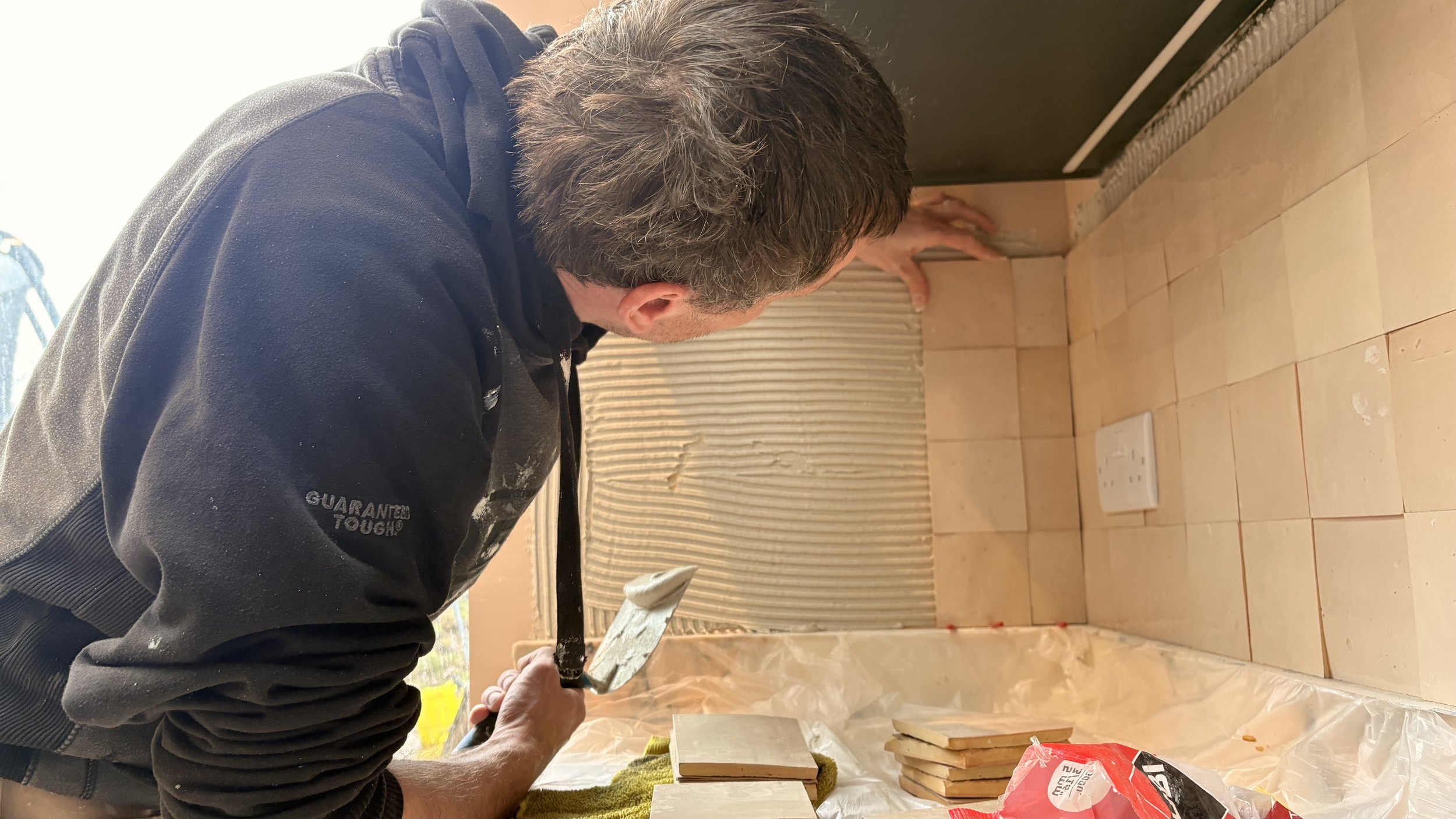 Tiler applying zellige tiles as a back splash to a kitchen. Tiles are mosaic factory and pale pink.