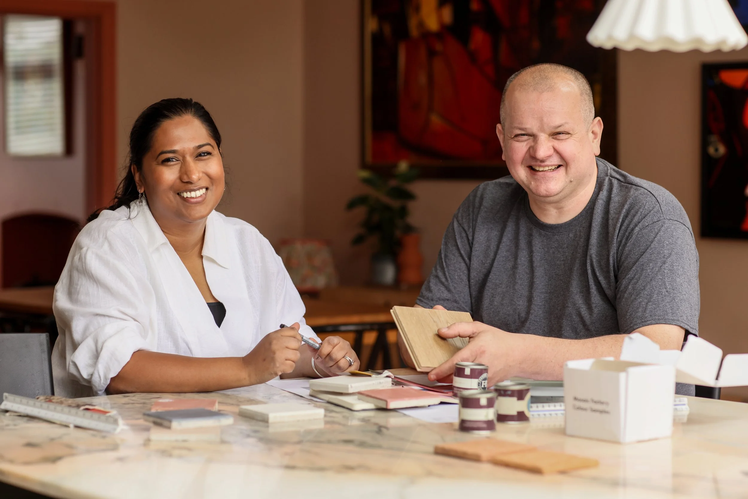Stave's co-founders, Shyamoli Burman Saha (designer) and Marcin Marynczak (master carpenter), seated at the marble island with paint, tile and timber samples laid out in front of them.