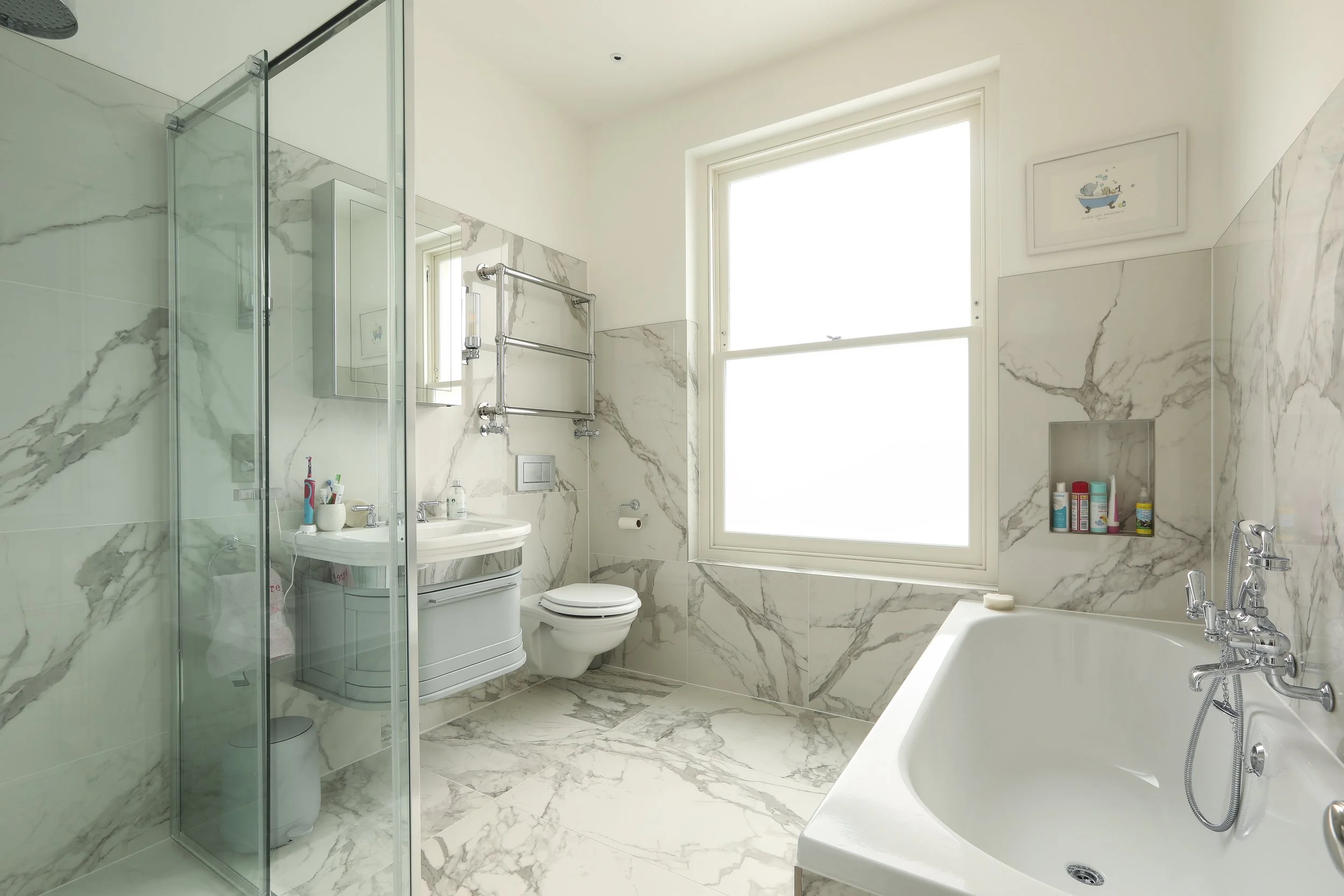 Modern white bathroom with marble walls and floor, large window, bathtub, toilet, sink, and shower area with glass door.