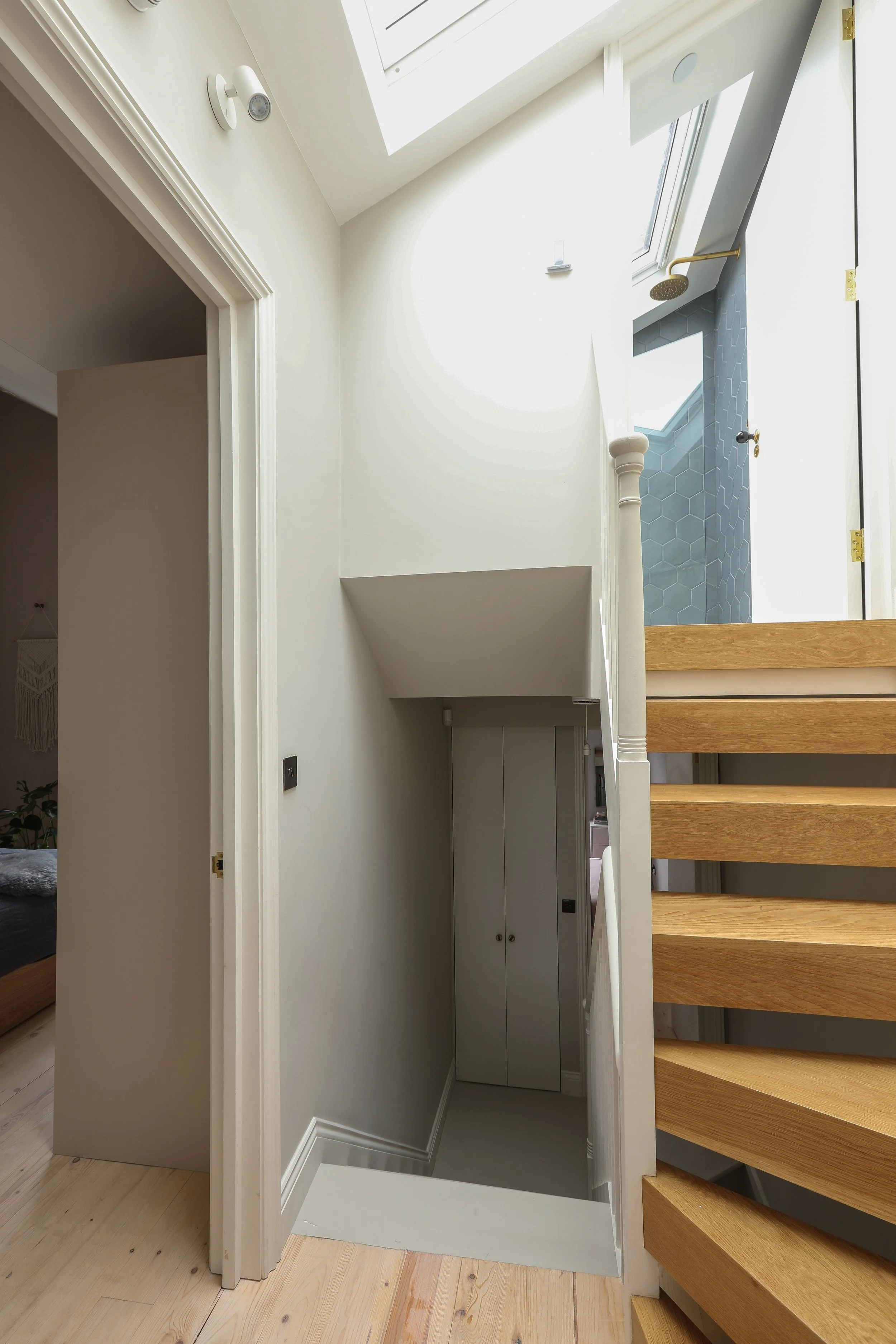 Interior view of a staircase with wooden steps and a white railing next to a gray wall with honeycomb tiles, an upper skylight window allowing natural light, and a small storage cabinet at the bottom of the stairs.