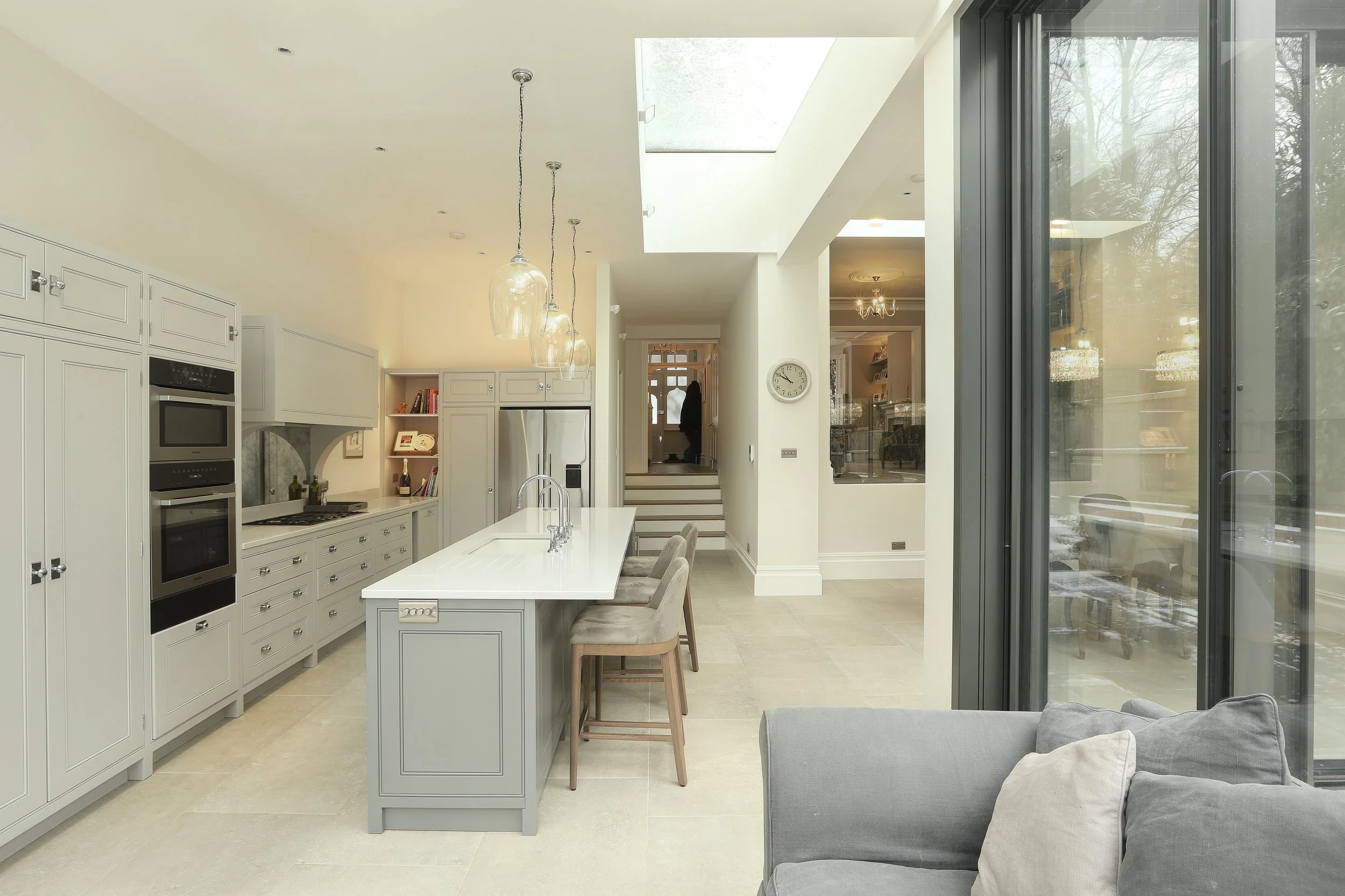 Modern kitchen with white cabinets, a large island, and bar stools. A sliding glass door opens to an outdoor area.