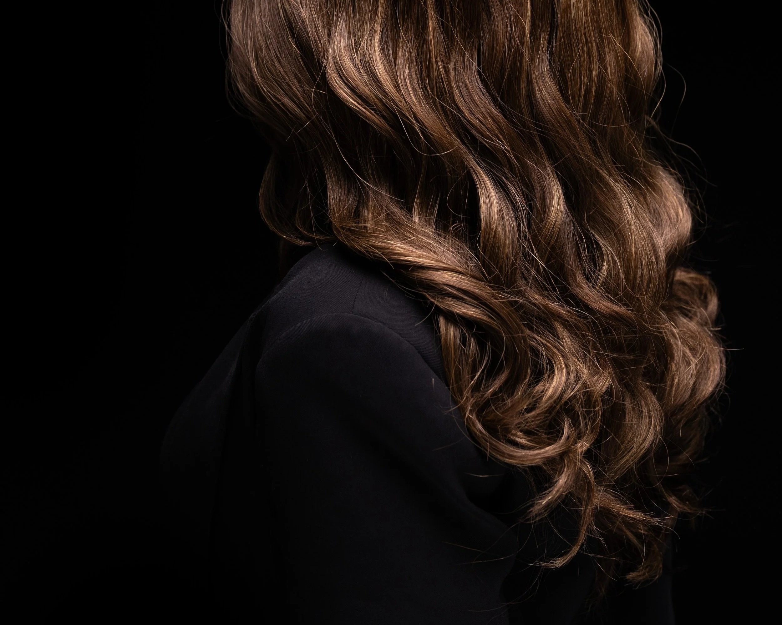 Close-up of wavy auburn hair against a black background.