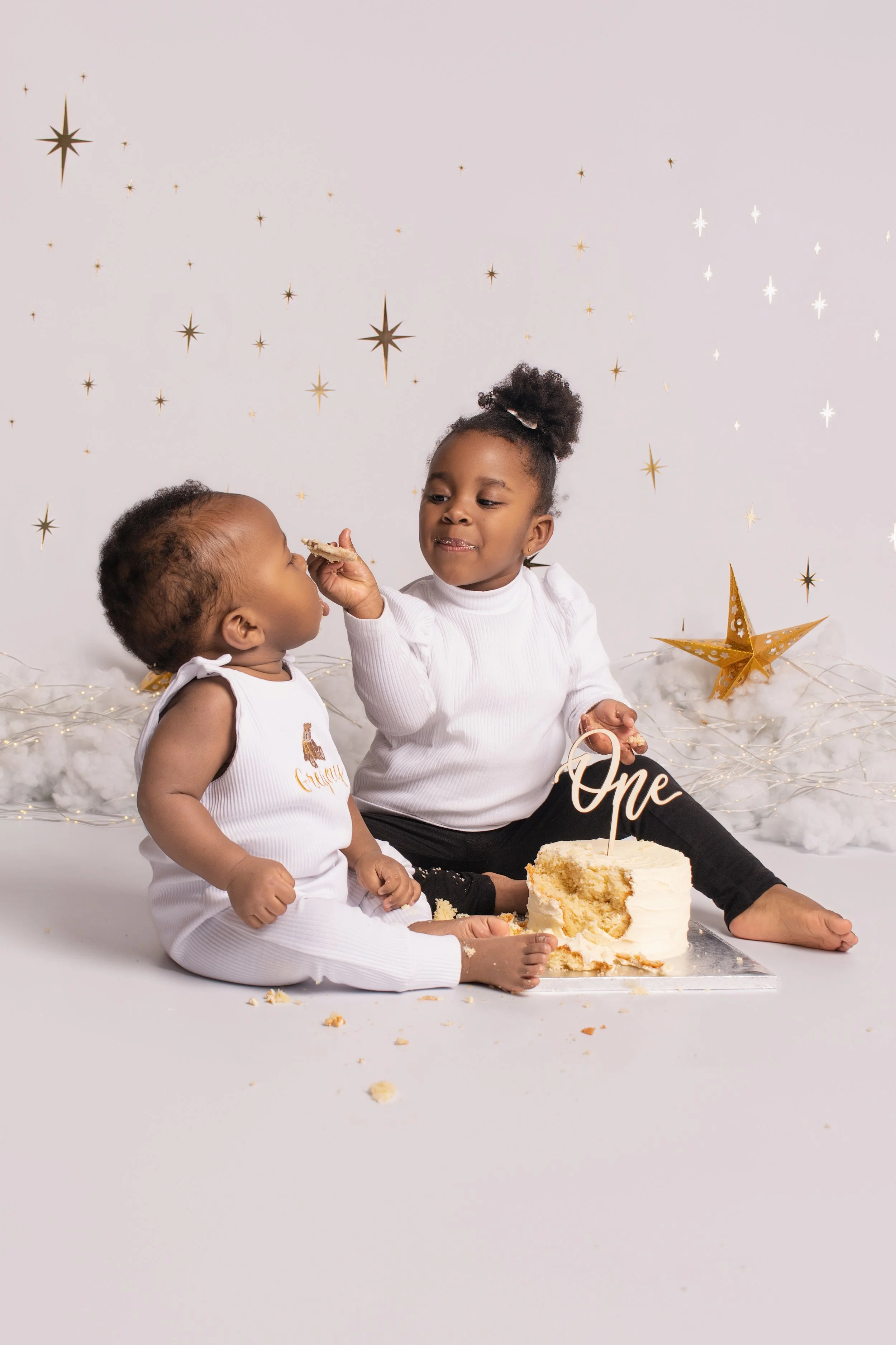 Two young children celebrating a first birthday, with a partially eaten cake and a