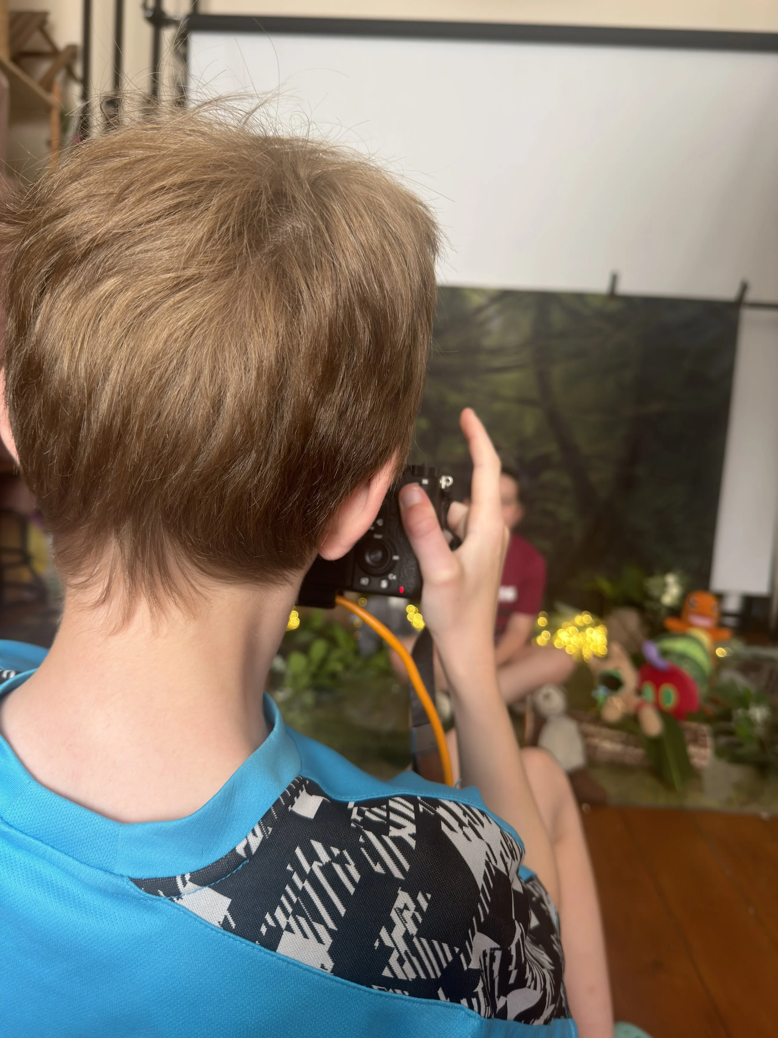 boy holding a camera, capturing a jungle themed backdrop.