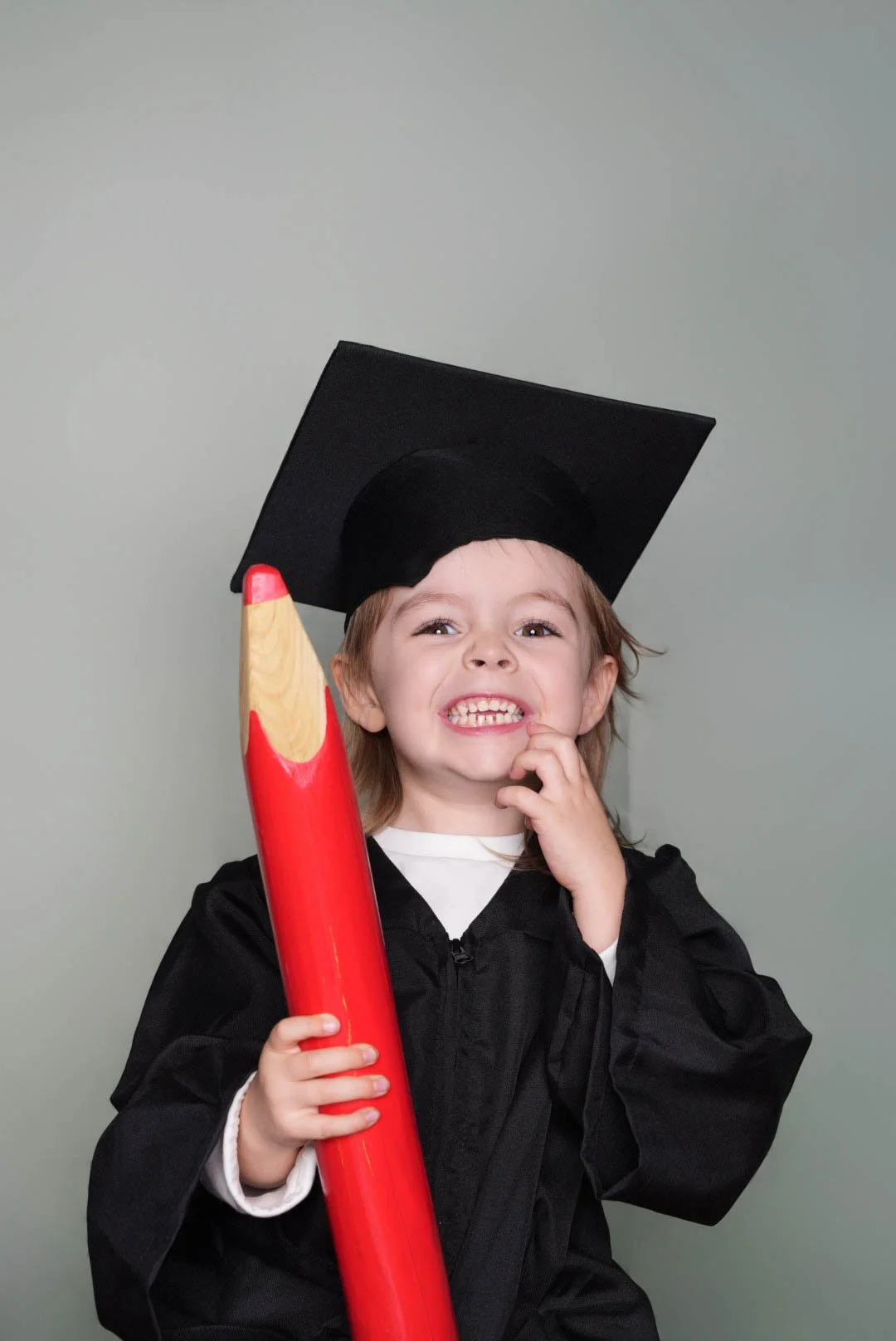 a-little-girl-in-a-graduation-gown-holding-a-red-pencil.jpg