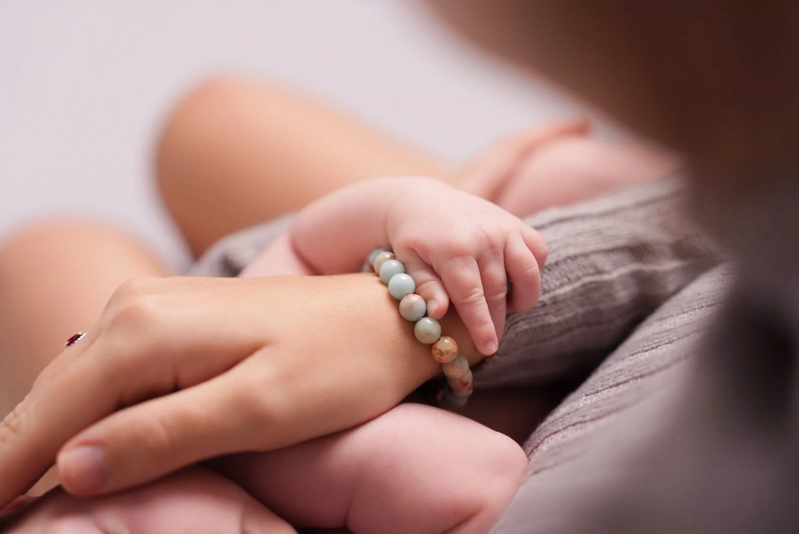 Close-up of a small child's hand holding an adult's hand, both wearing beaded bracelets, with a soft background.