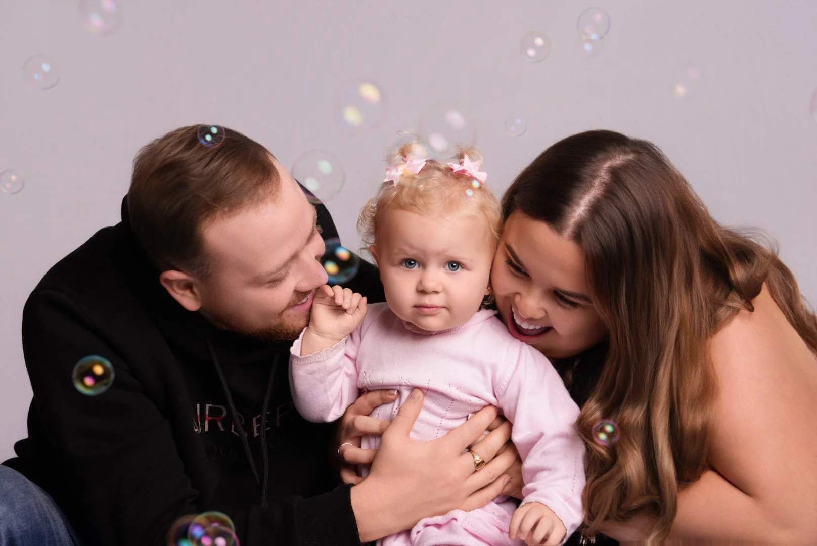 A family with a man, woman, and a young girl sitting together, surrounded by soap bubbles.