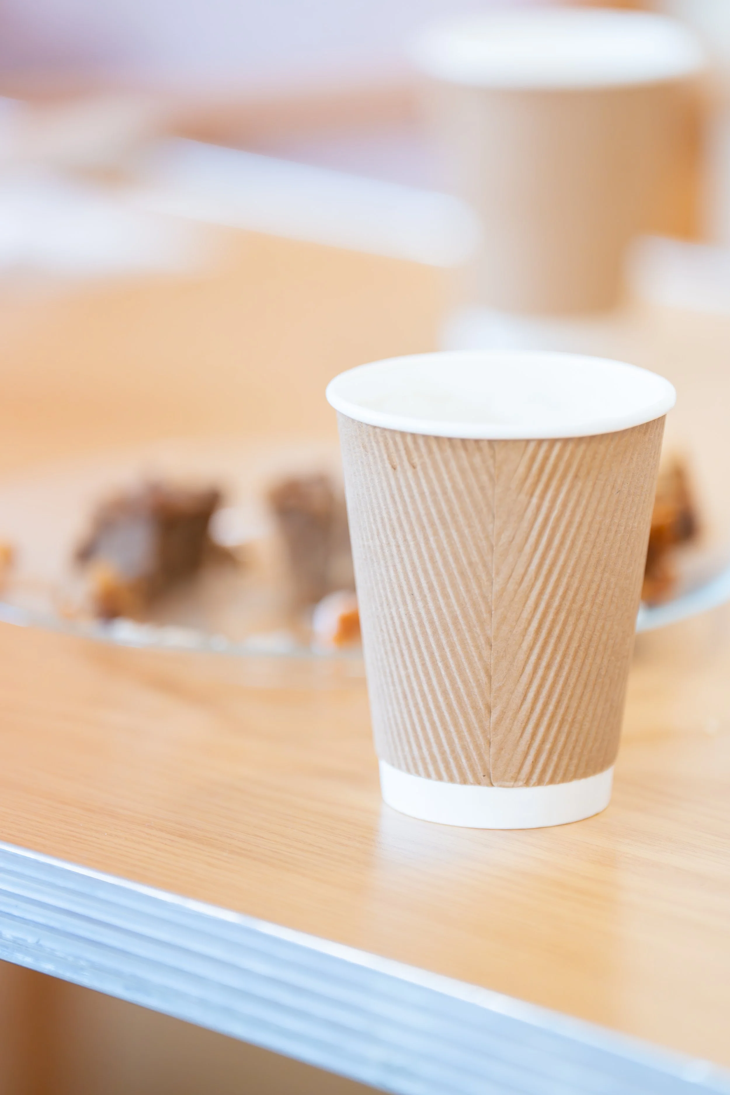 Coffee cup on a table with some cake in the background