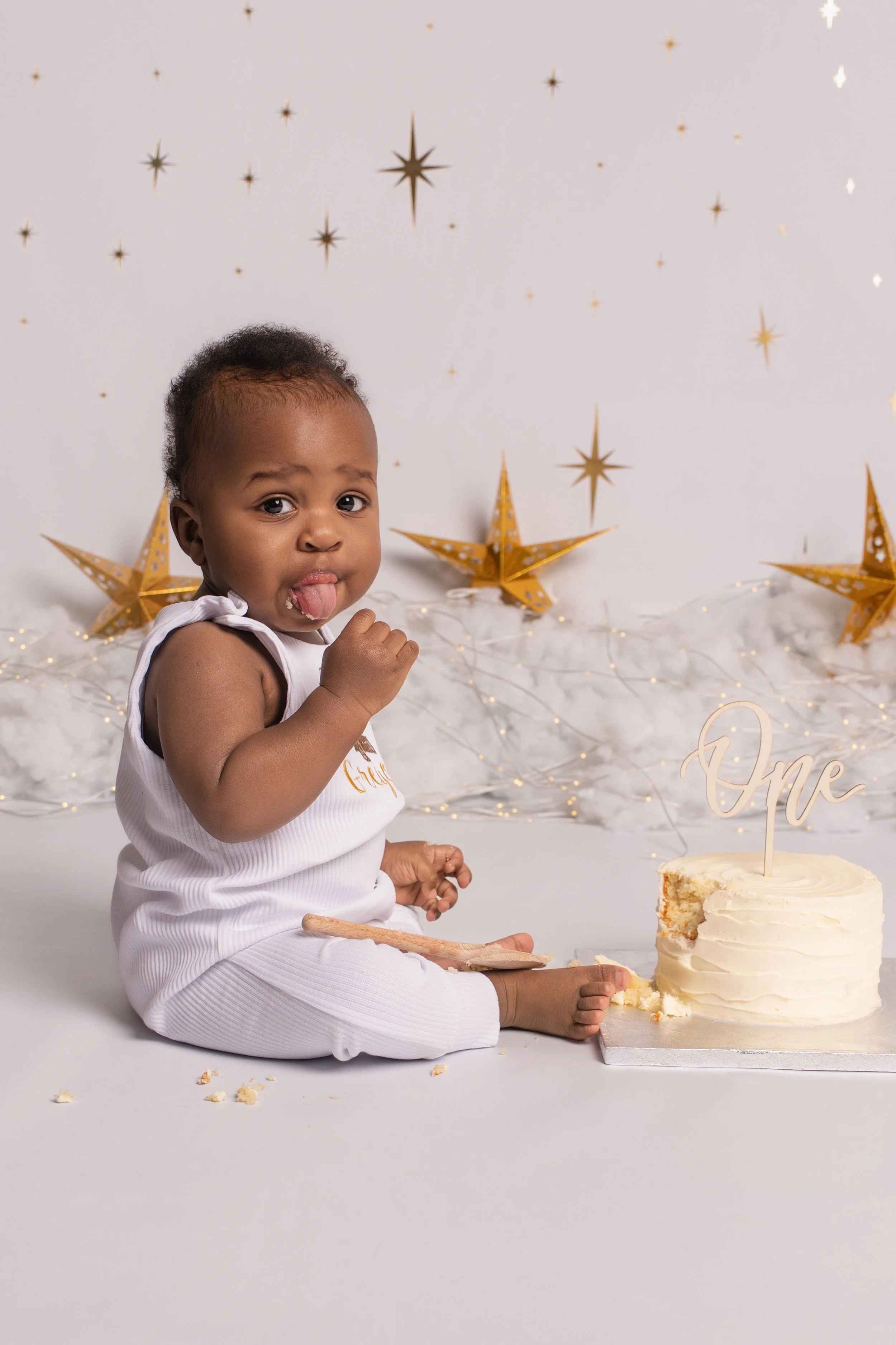 A baby celebrating their first birthday with a small cake, surrounded by gold star decorations and festive lights.