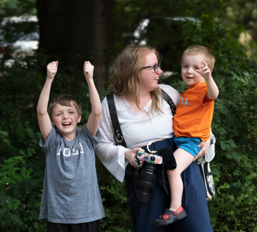 A woman with glasses, two young boys, and a green outdoor background.