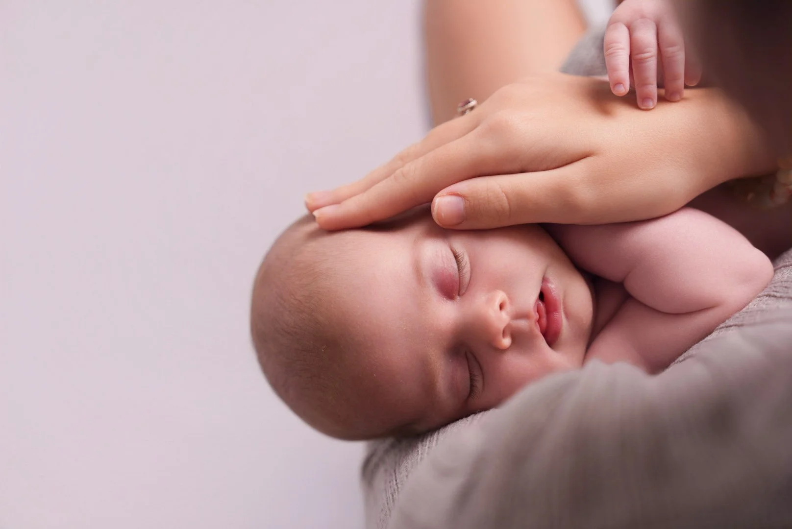 Close-up of a sleeping baby with eyes closed, resting on a person's shoulder while being gently touched on the head.