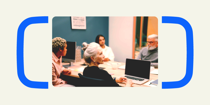 A group of four people in a meeting room with laptops, sitting at a table engaging in discussion.