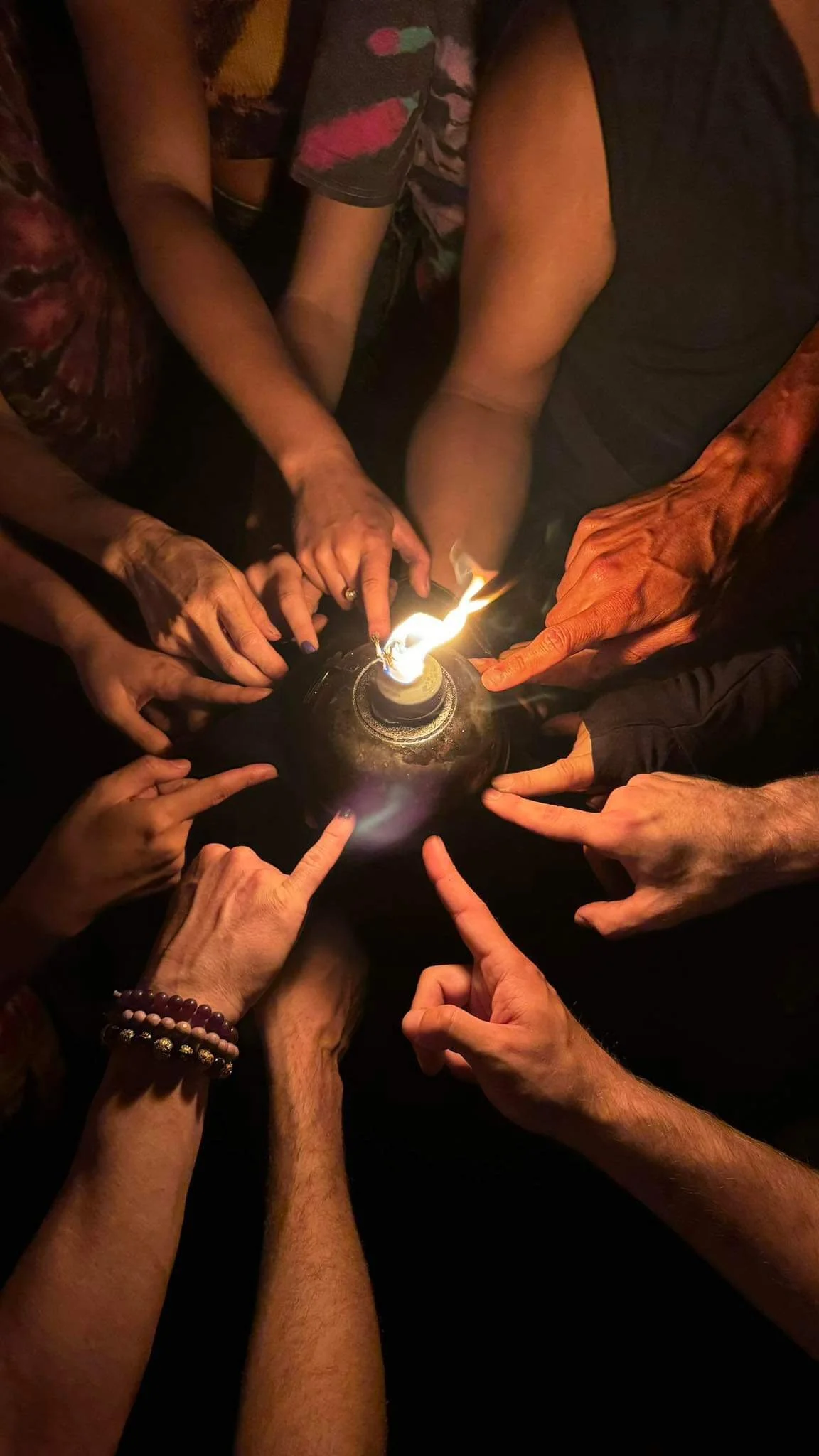 Multiple hands pointing at a flame burning on a small round object