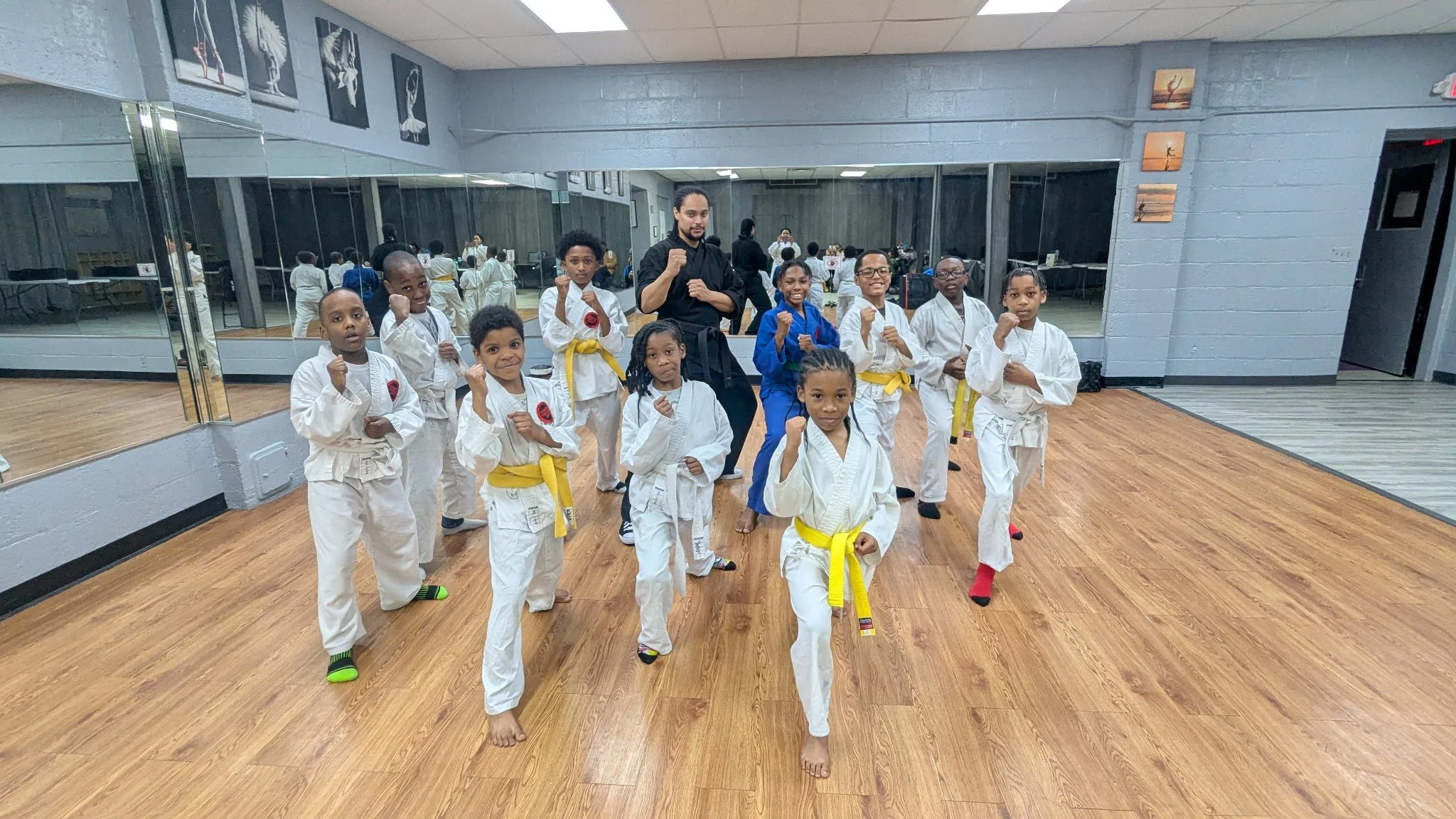 Group of children in martial arts uniforms posing with their instructors in a dojo, performing martial arts stances.