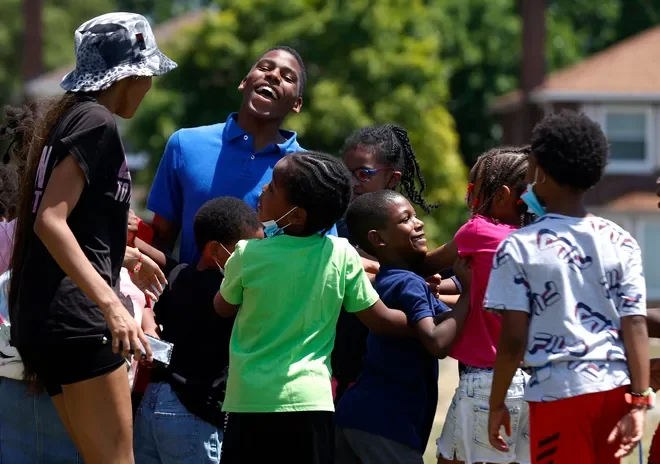 A group of children and a young adult laughing and playing outside on a sunny day.
