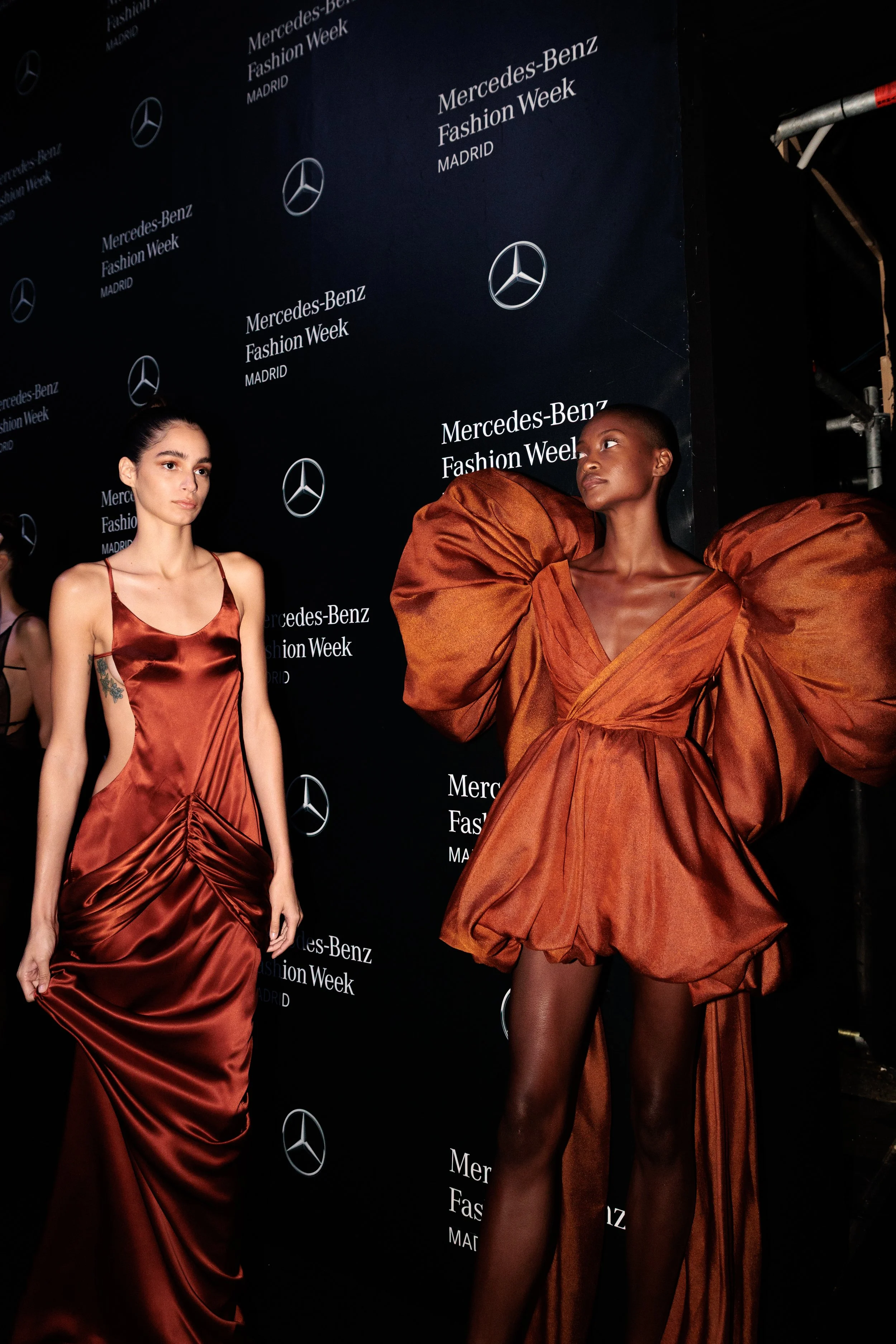 Dos modelos en pasarela durante la Mercedes-Benz Fashion Week en Madrid, con fondo negro con logos de Mercedes-Benz y texto en blanco.