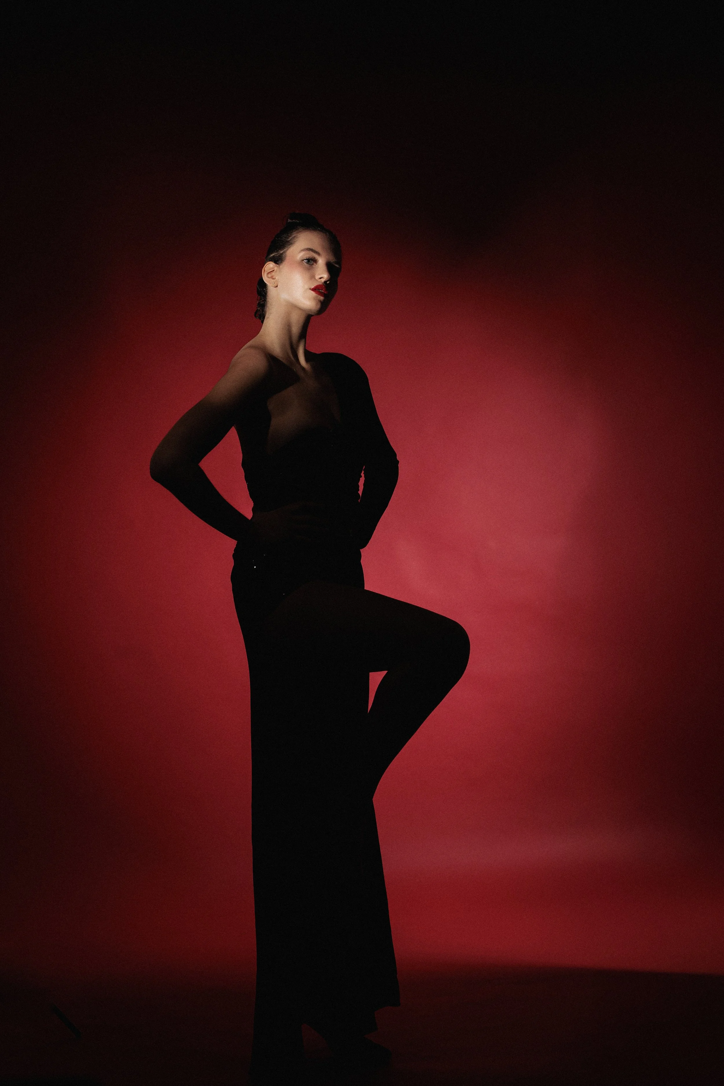 Mujer posando en fondo rojo, vestimenta negra, peinado recogido, maquillaje llamativo.