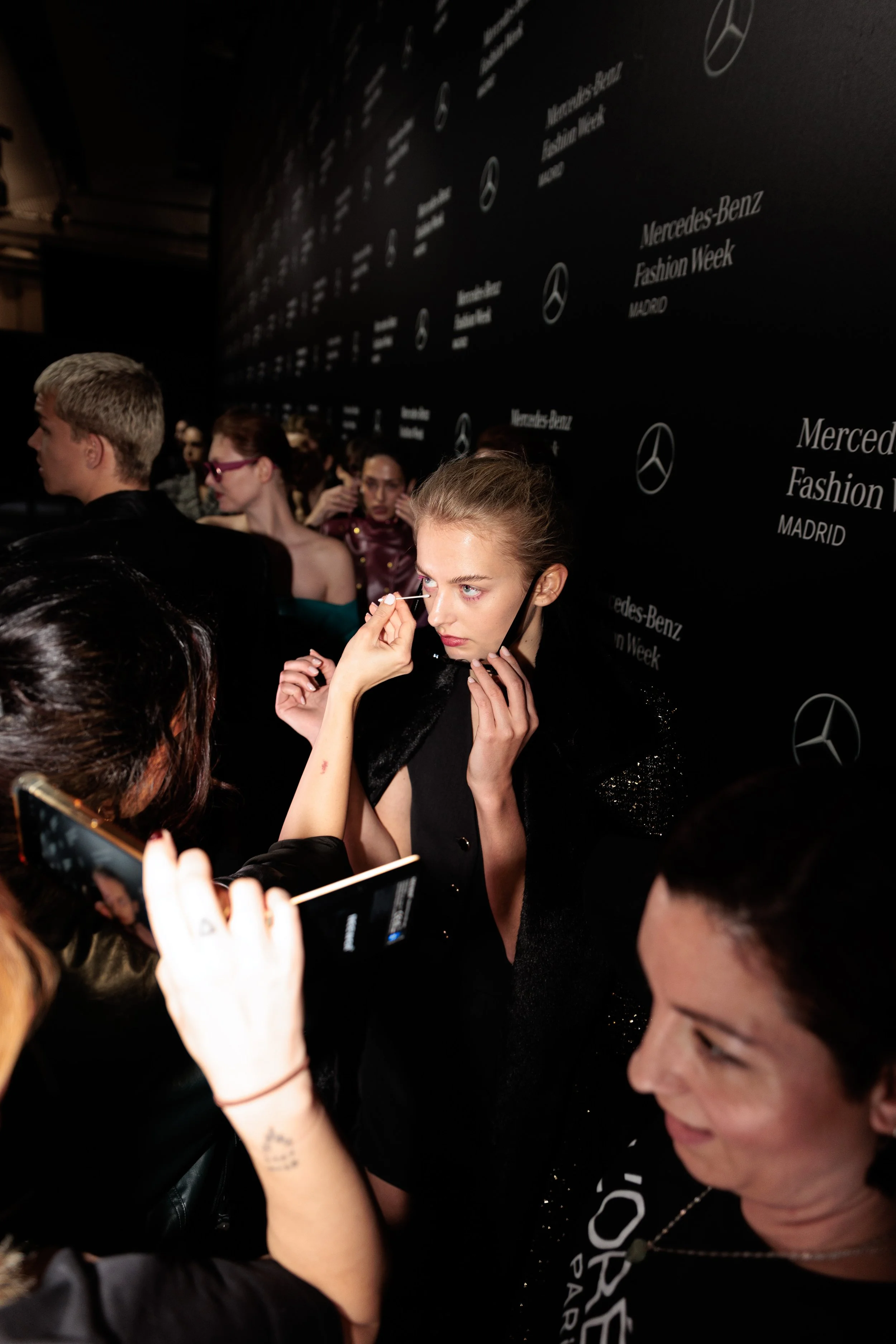 Una modelo se maquilla en un evento de Mercedes-Benz Fashion Week en Madrid, rodeada de varias personas.
