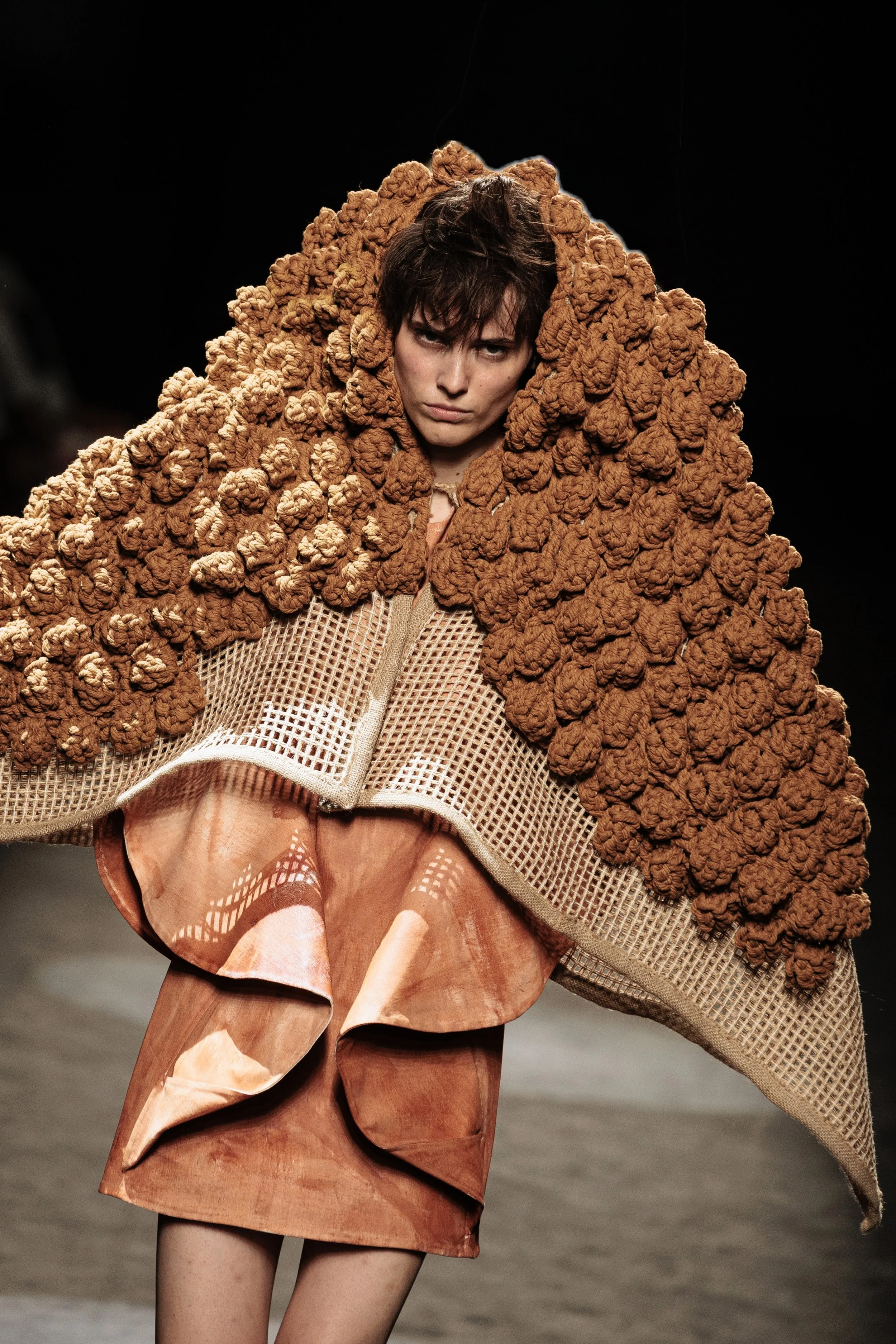 Modelo en pasarela con vestido y mantón de lana con texturas y colores terrosos.