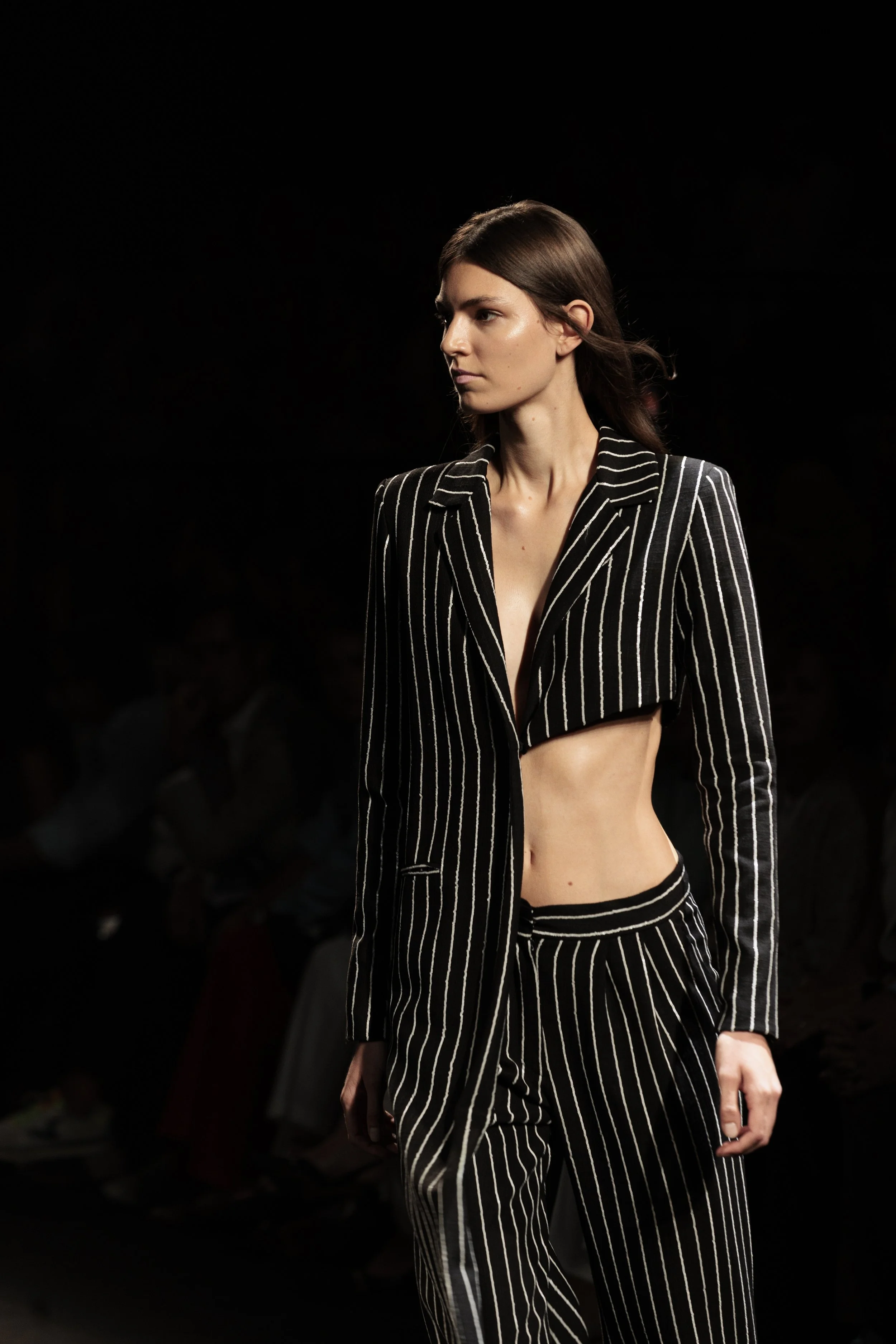 Mujer con cabello castaño oscuro y vestido a rayas negras y blancas, posando en pasarela de moda.