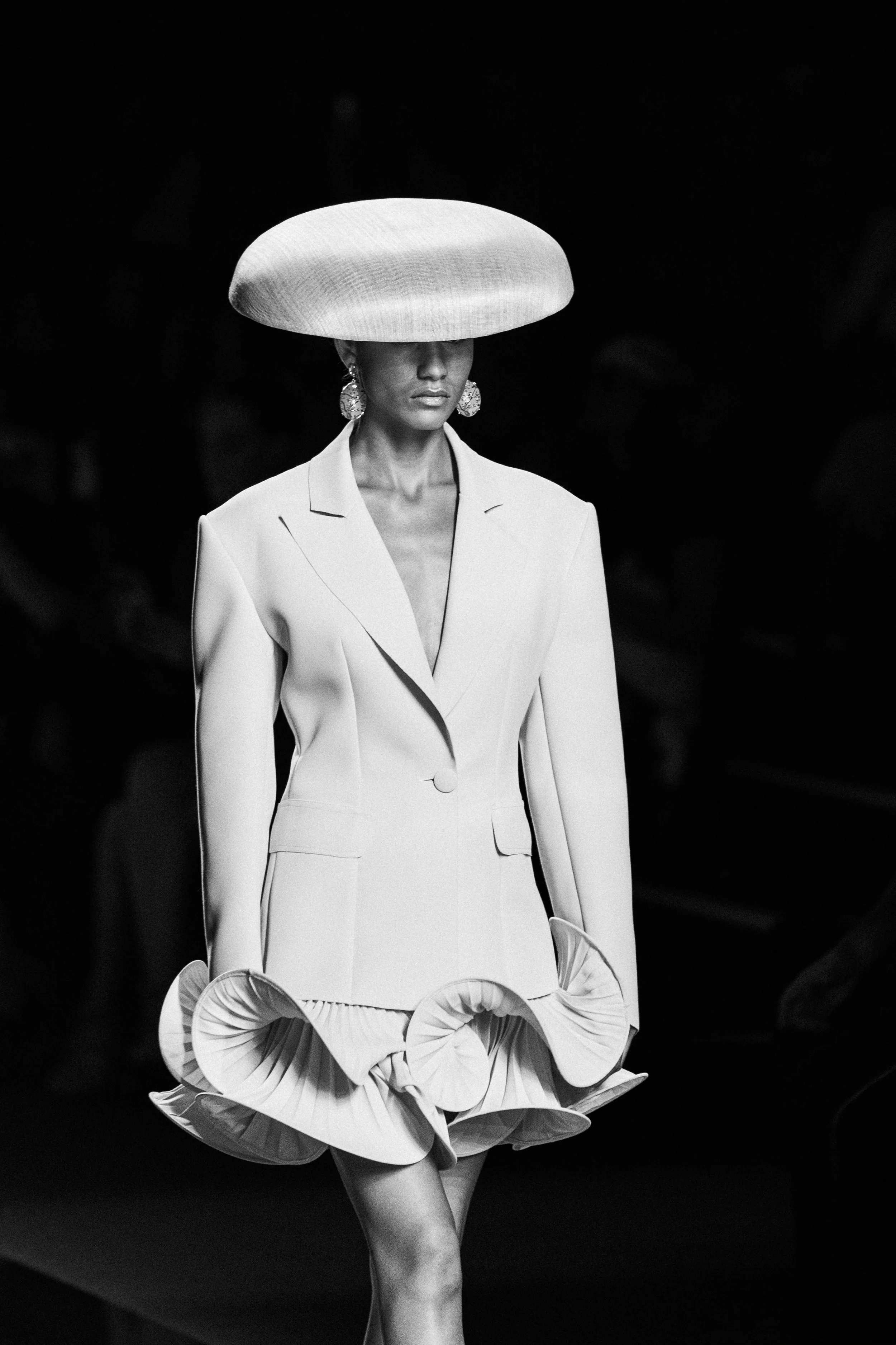 Modelo con sombrero grande y vestido de moda en pasarela de moda.