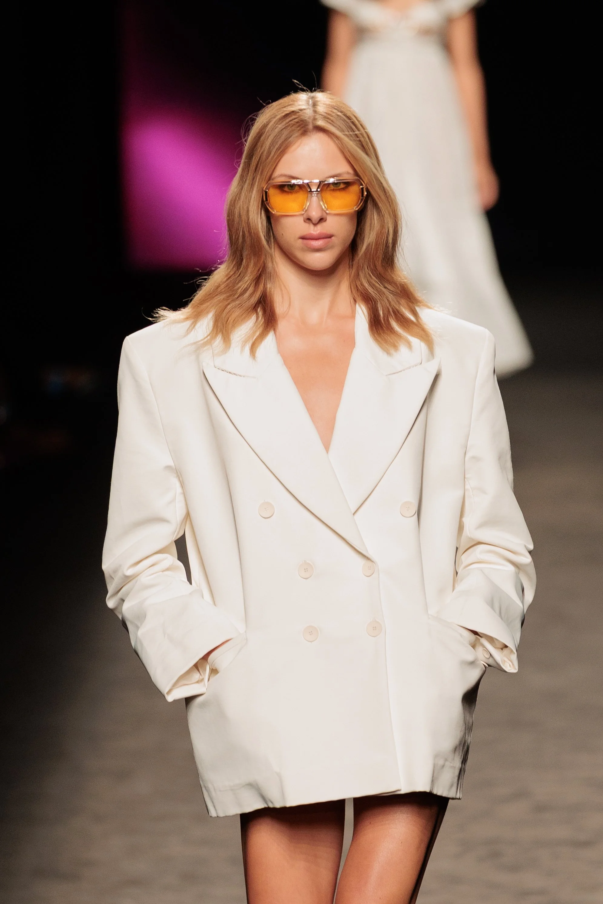 Mujer caminando en pasarela con blazer blanco y gafas de sol amarillas