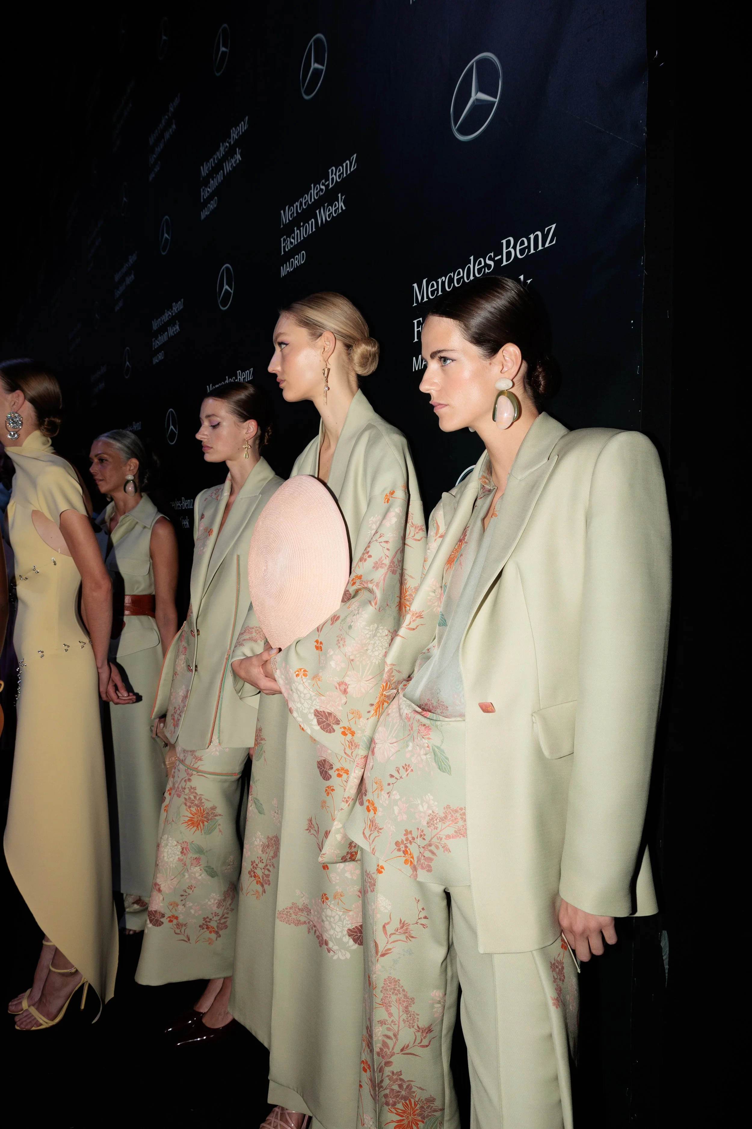 Modelos en pasarela en Mercedes-Benz Fashion Week Madrid, luciendo ropa elegante en tonos beige y accesorios llamativos.