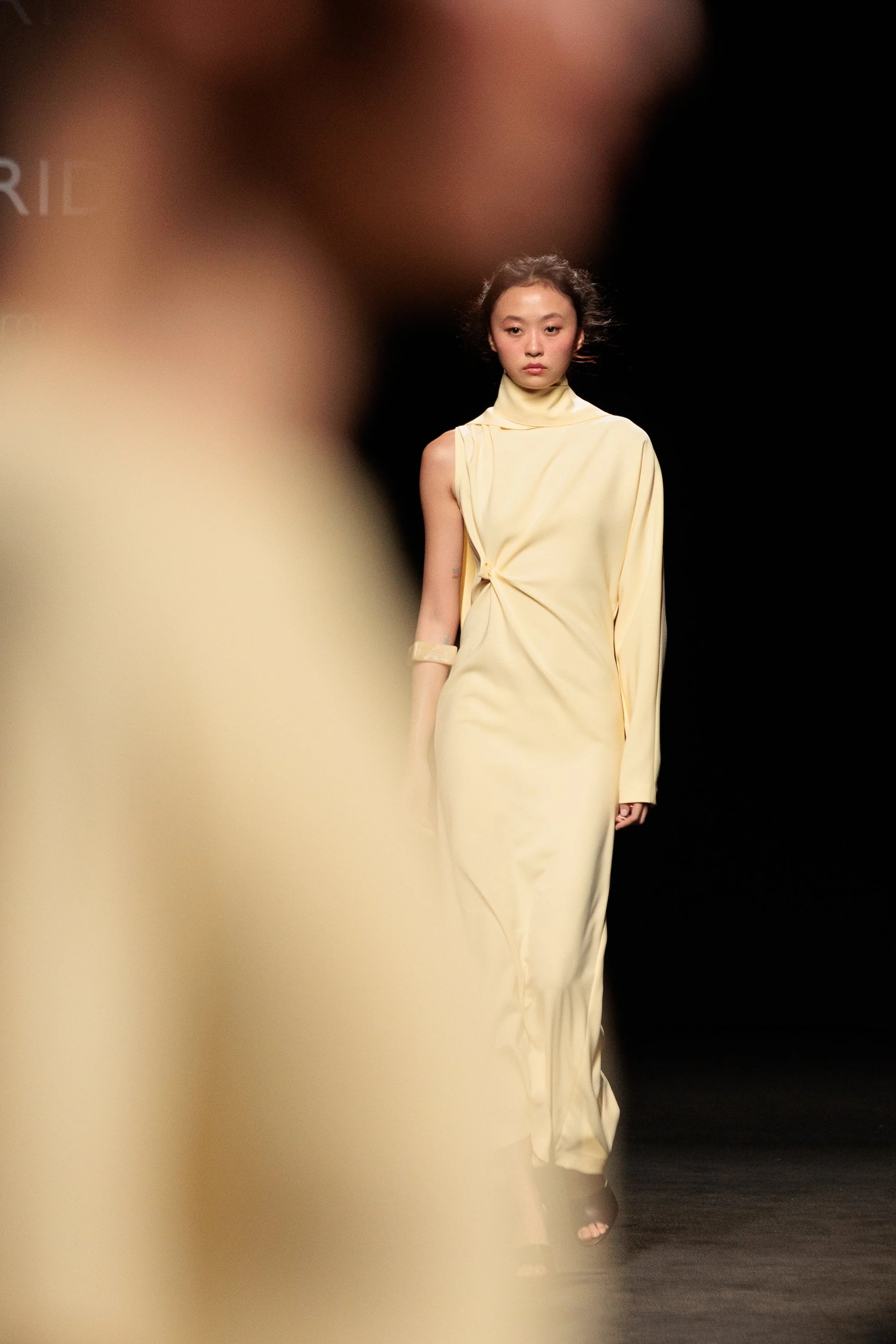 Modelo desfilando en la pasarela con vestido largo color crema.