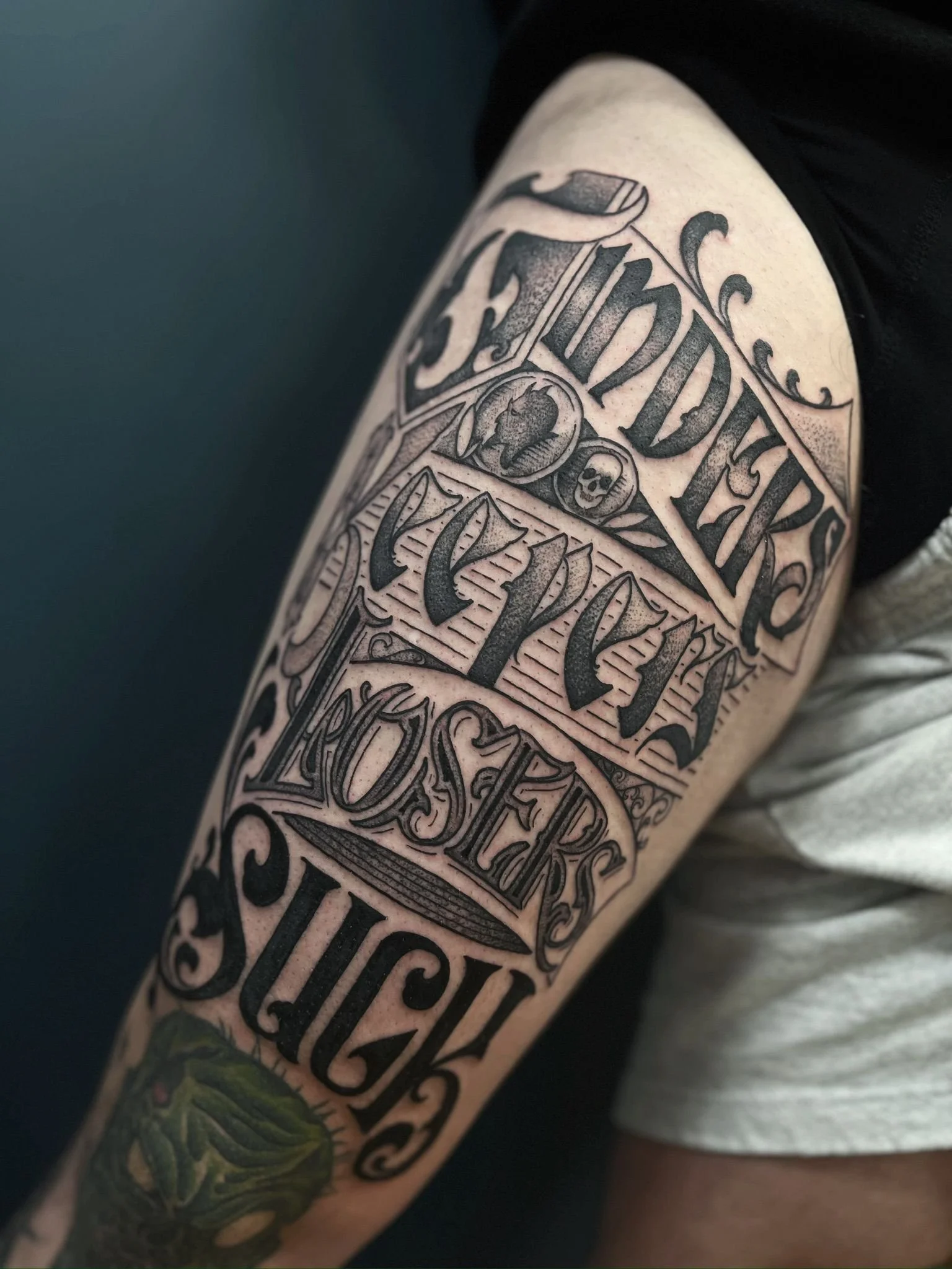 Tattoo on person's arm with words 'FINDERS KEEPERS, LOSERS SUCK,’ in bold, detailed lettering, with some decorative elements and small icons.