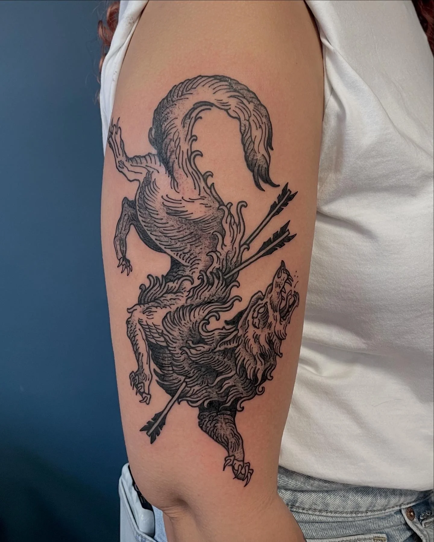 Black tattoo on person's upper arm depicting a wolf with arrows.