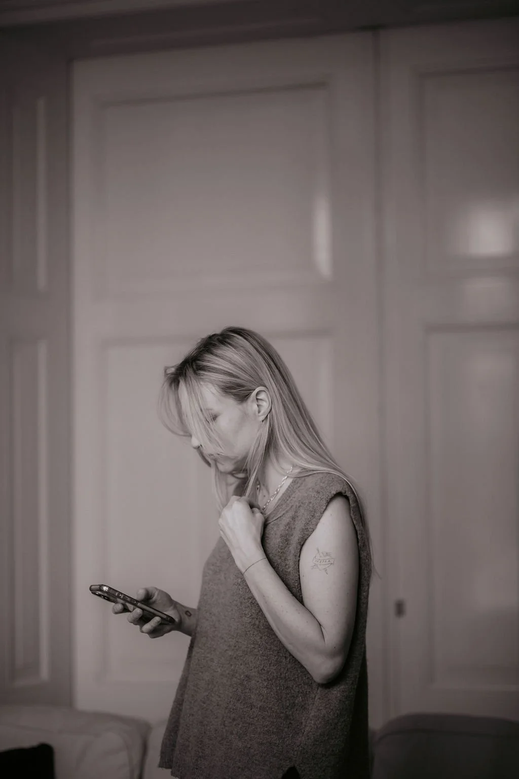 Vrouw met lang haar kijkt op haar smartphone, in een grijze mouwloze top, binnen, zwart-wit