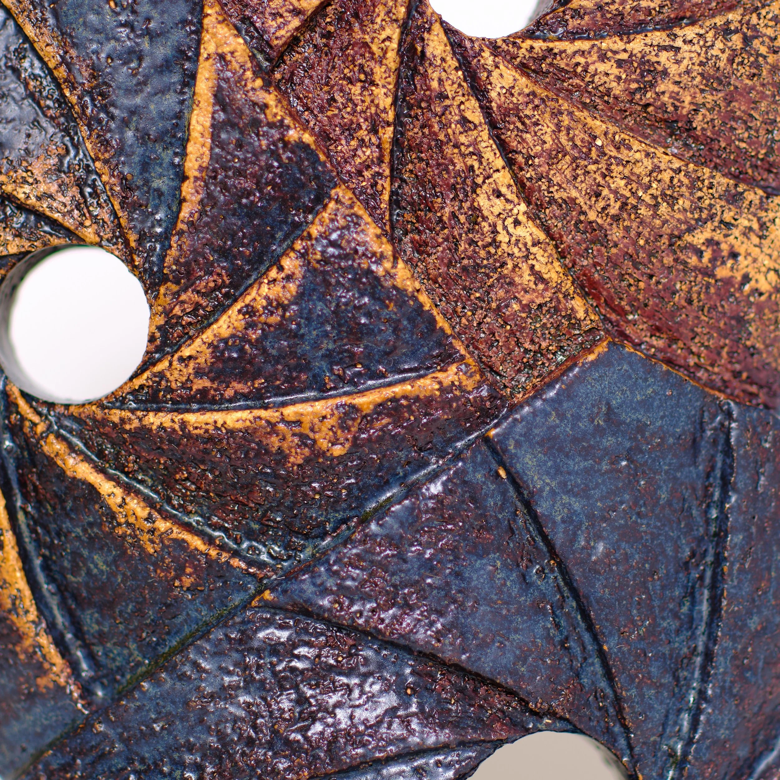 Close-up of a ceramic sculpture with dark and rusty orange colours, showing deep textured grooves.