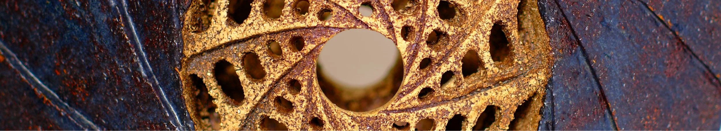 Close-up of a carved ceramic sculpture featuring an outer ring of dark blue, with a clockwise spiralling design, and a pale beige inner circle featuring an anticlockwise spiralling design, with small oval holes carved through the hollow sculpture.