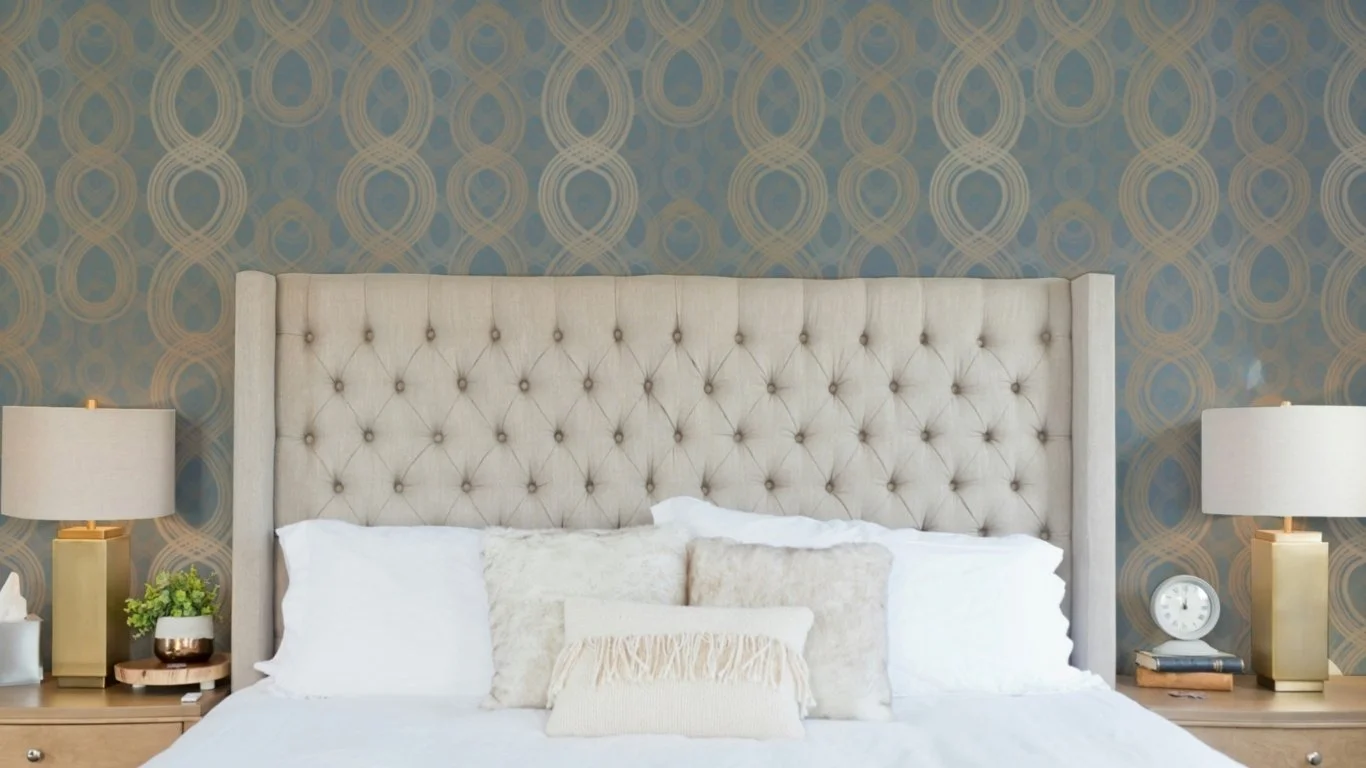 Tufted bed styled against slate blue Majestic Ovals wallpaper featuring layered oval rings in warm neutral tones.
