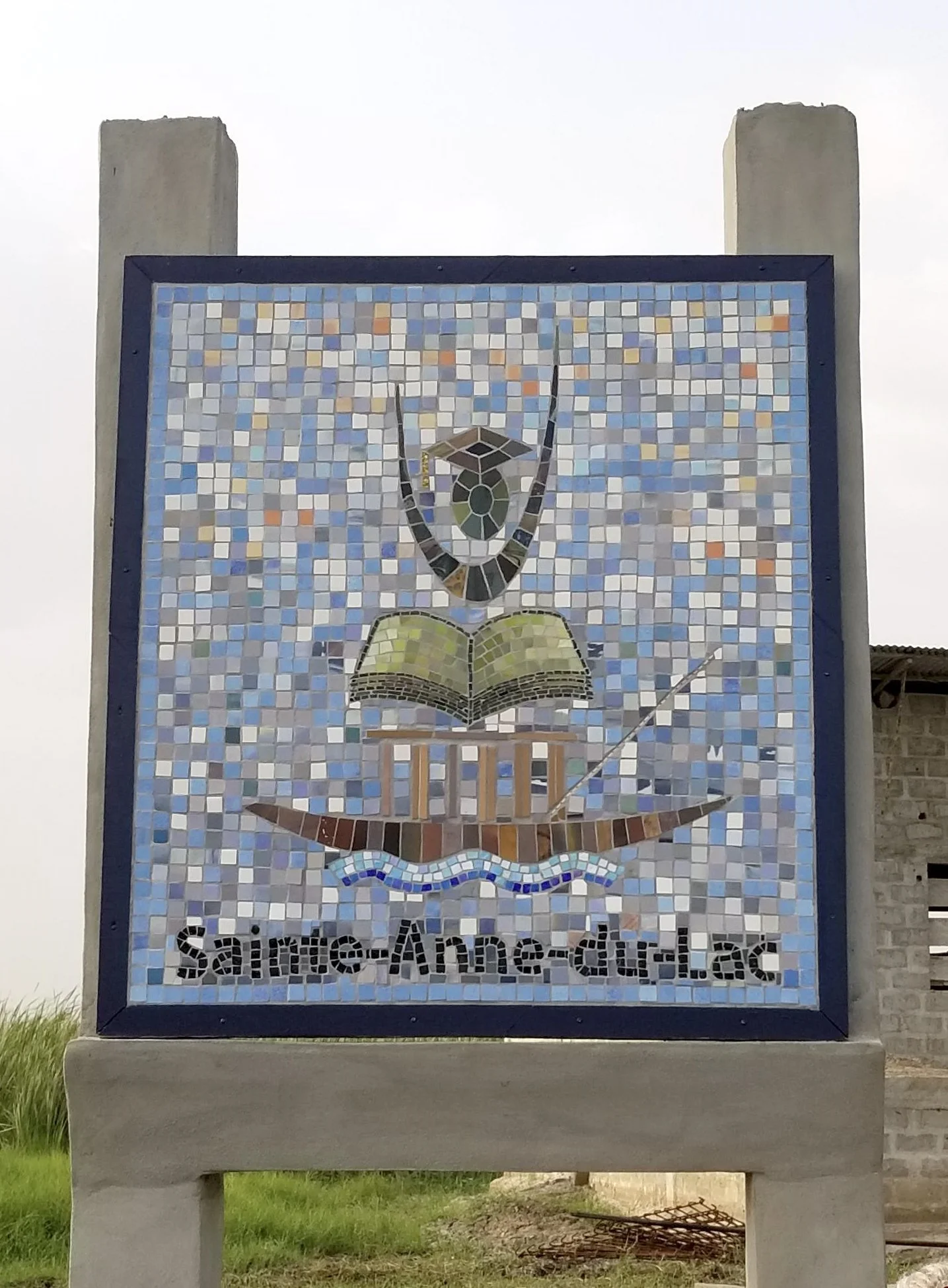 Panneau en mosaïque avec une image d'une main tenant un livre et un geste de prière, avec le texte 'Saintes Ange Gardien' en bas.