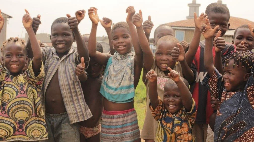 Groupe d'enfants africains souriants et levant les bras dans un espace extérieur.