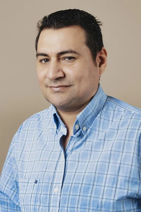 A man wearing a blue plaid shirt poses in front of a beige background