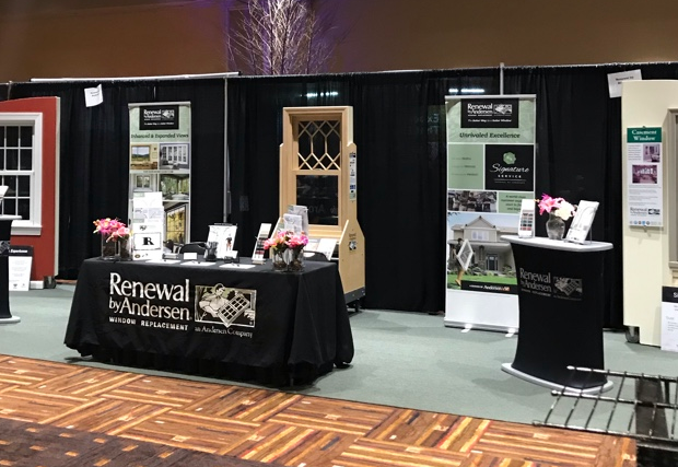Exhibition booth displaying window replacement services with samples, promotional materials, and flowers.