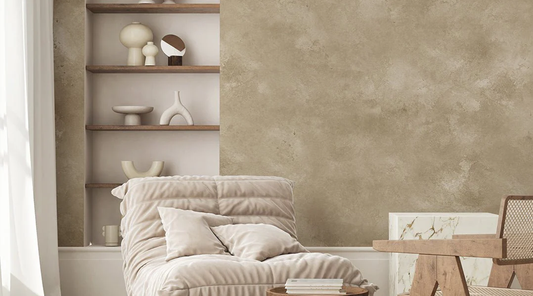 A cozy living room corner with beige plush chair, pillows, a wooden side table, a shelf with decorative vases, and a textured wall.