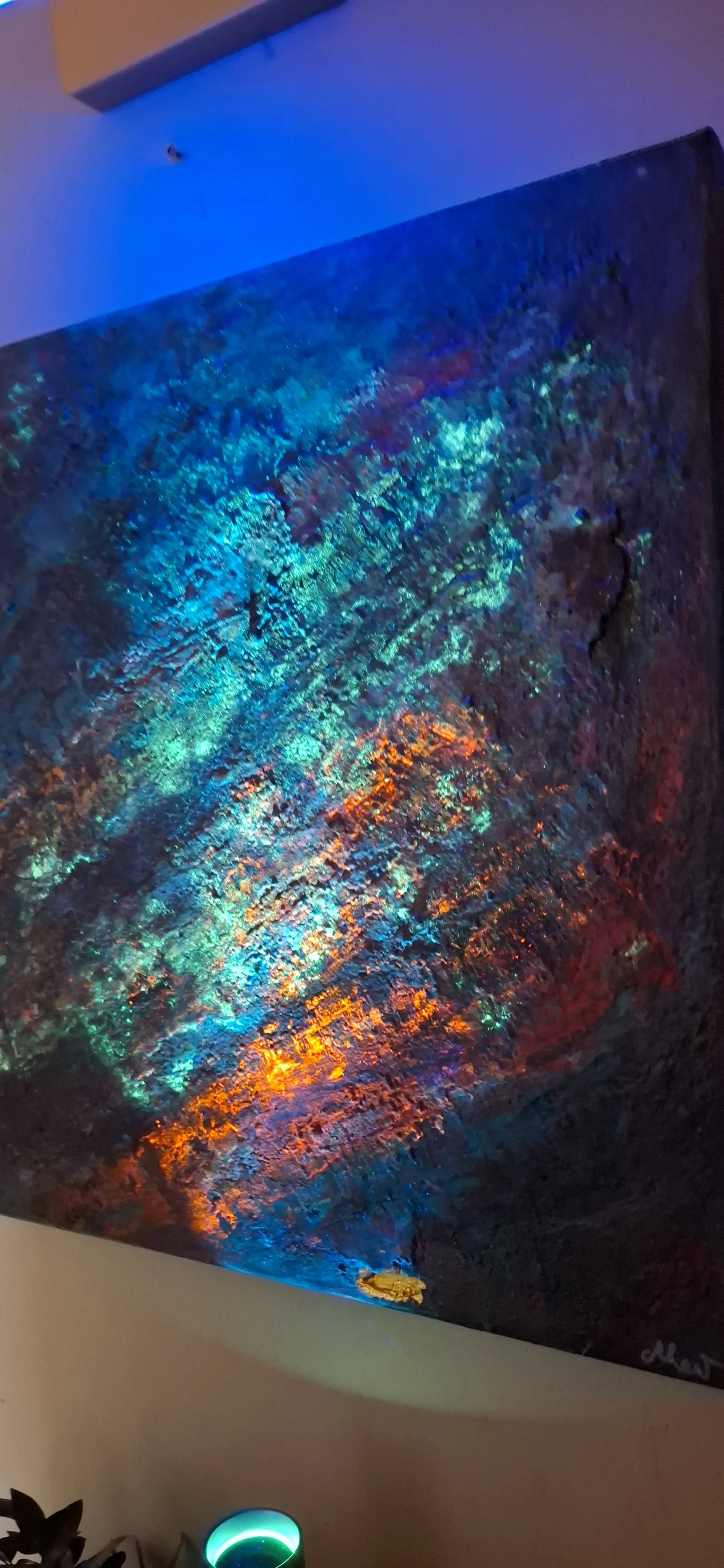 Ein abstraktes Kunstwerk mit leuchtenden, regenbogenartigen Farben und Struktur, das auf einer Wand hängt.