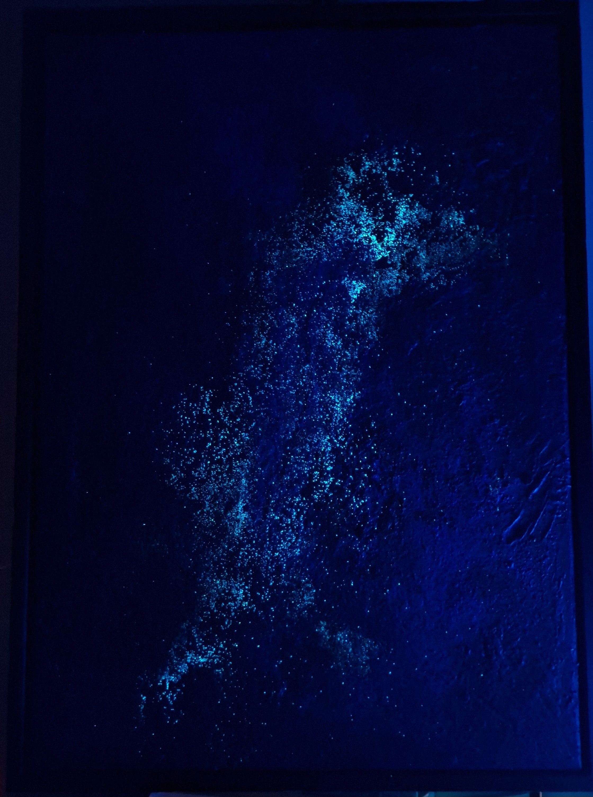 Blauer, leuchtender Punkt aus Staub oder Glitzer vor dunklem Hintergrund, schimmert im Licht.