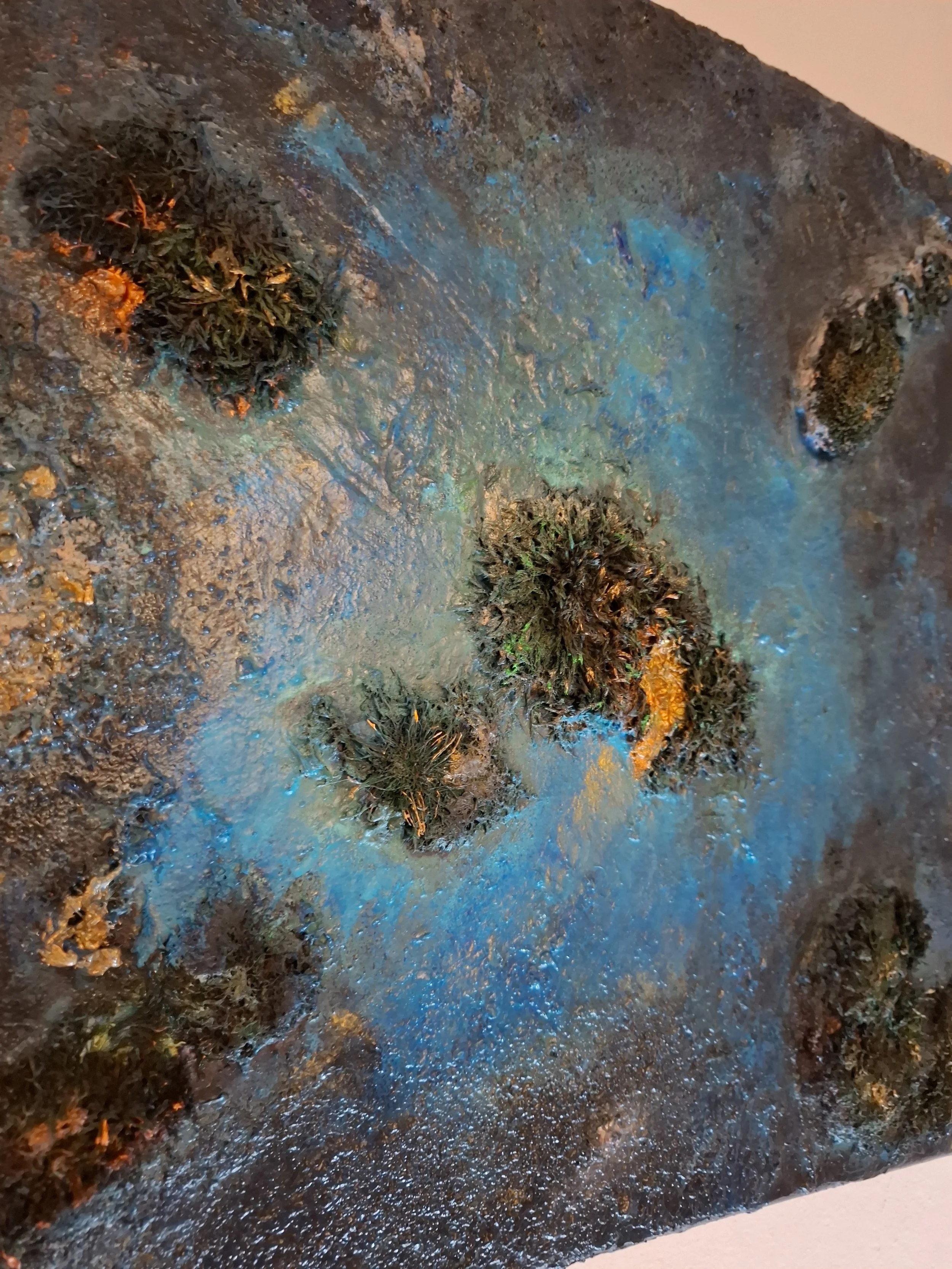 Kunstwerk mit bunten, texturierten Flächen und mehreren kleinen, dichten, dunklen Pflanzen auf einer schwarzen Oberfläche mit blauen und grünen Farbtönen.