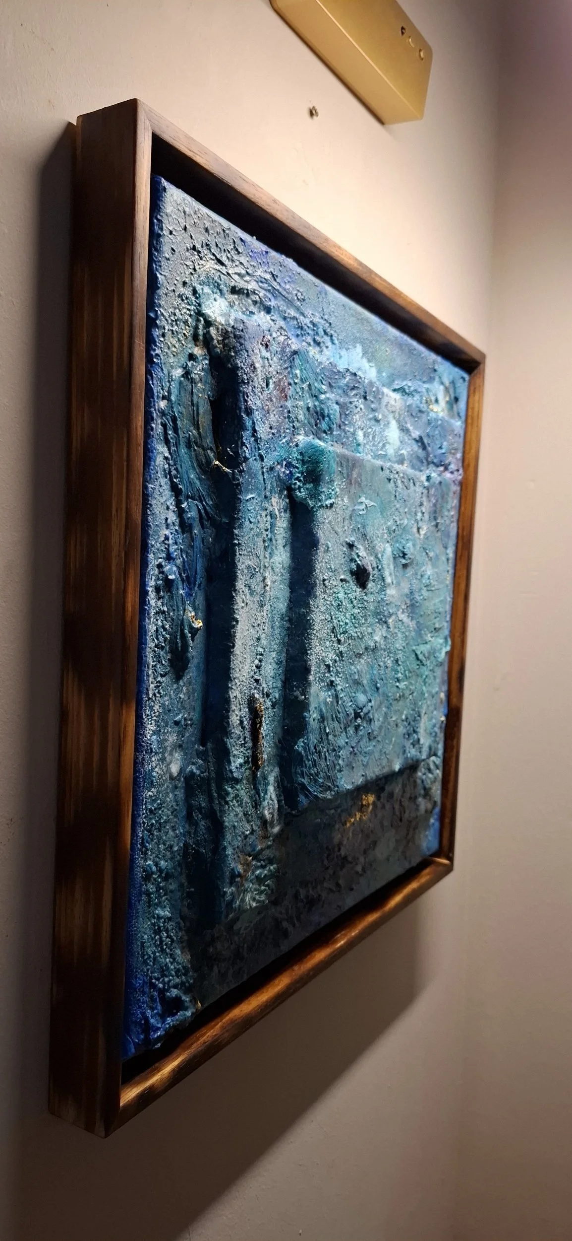 Abstraktes blauer Gemälde mit Holzrahmen, das an einer weißen Wand hängt.