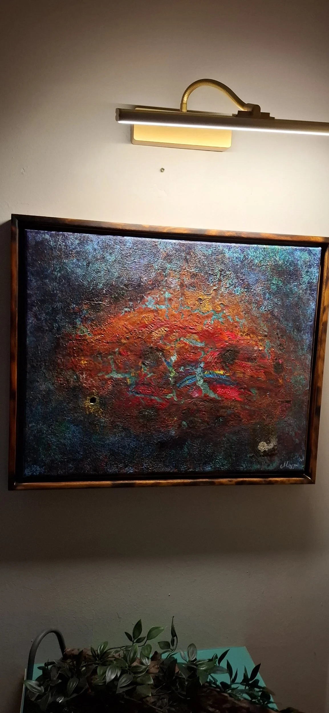 Abstrakes Gemälde mit dominanten Rottönen, blauen und grünen Akzenten, in einem Holzrahmen, beleuchtet durch eine Wandlampe darüber.