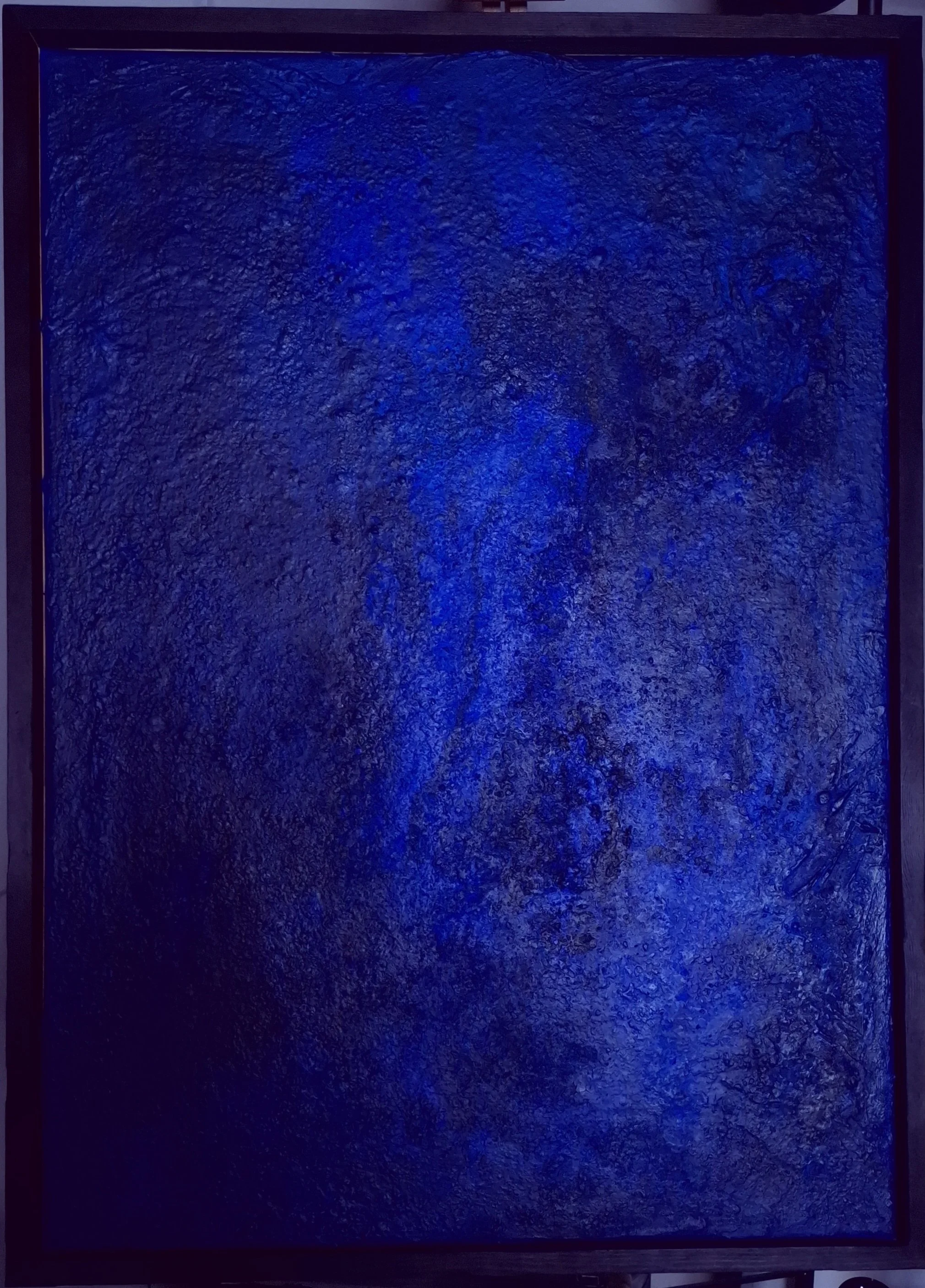 Ein dunkles, texturiertes quadratisches Kunstwerk mit blauen Lichtern, eingebettet in einen Rahmen.